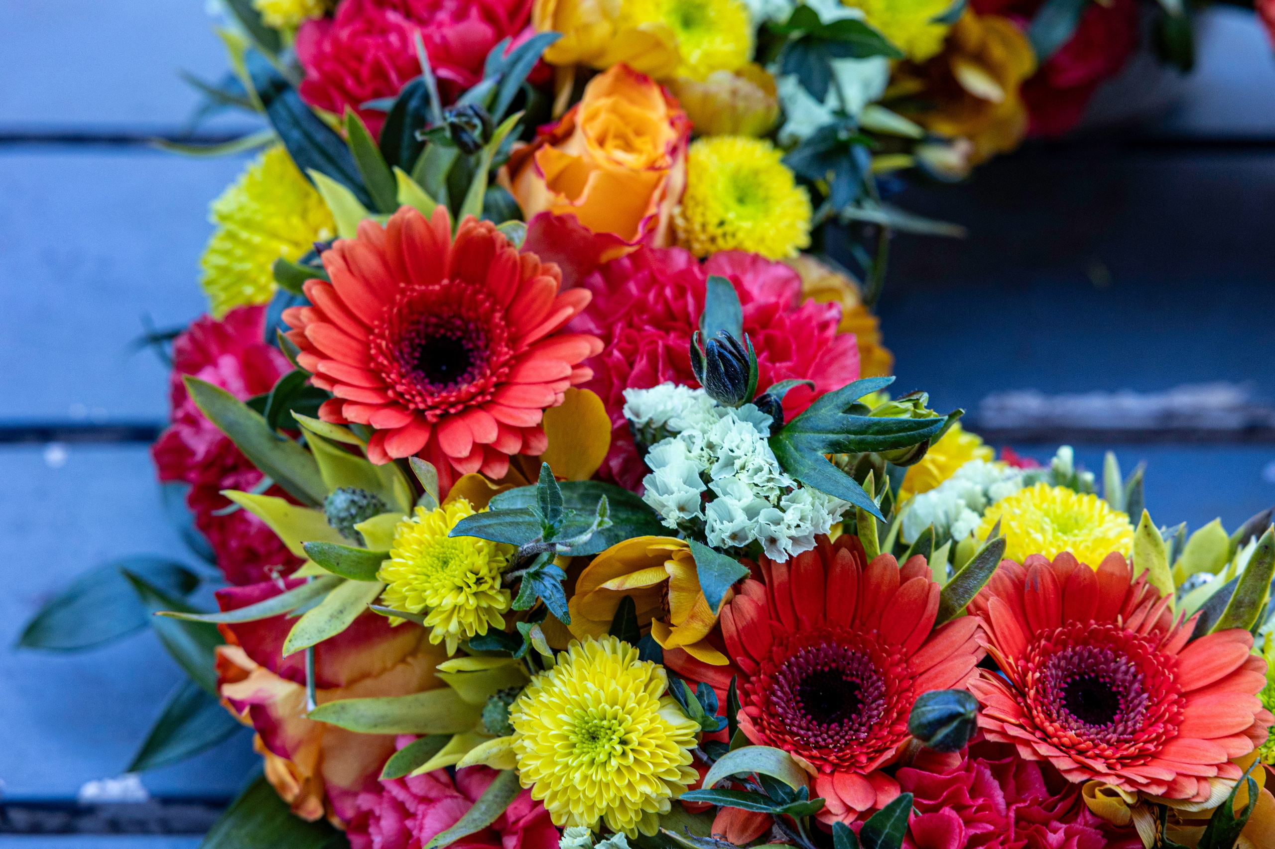Farverig begravelsesdekoration med smukke gerbera, roser og frodigt grønt. Akropolis Blomster skaber personlige blomsterhilsner, der formidler omsorg, kærlighed og tak ved den sidste afsked.