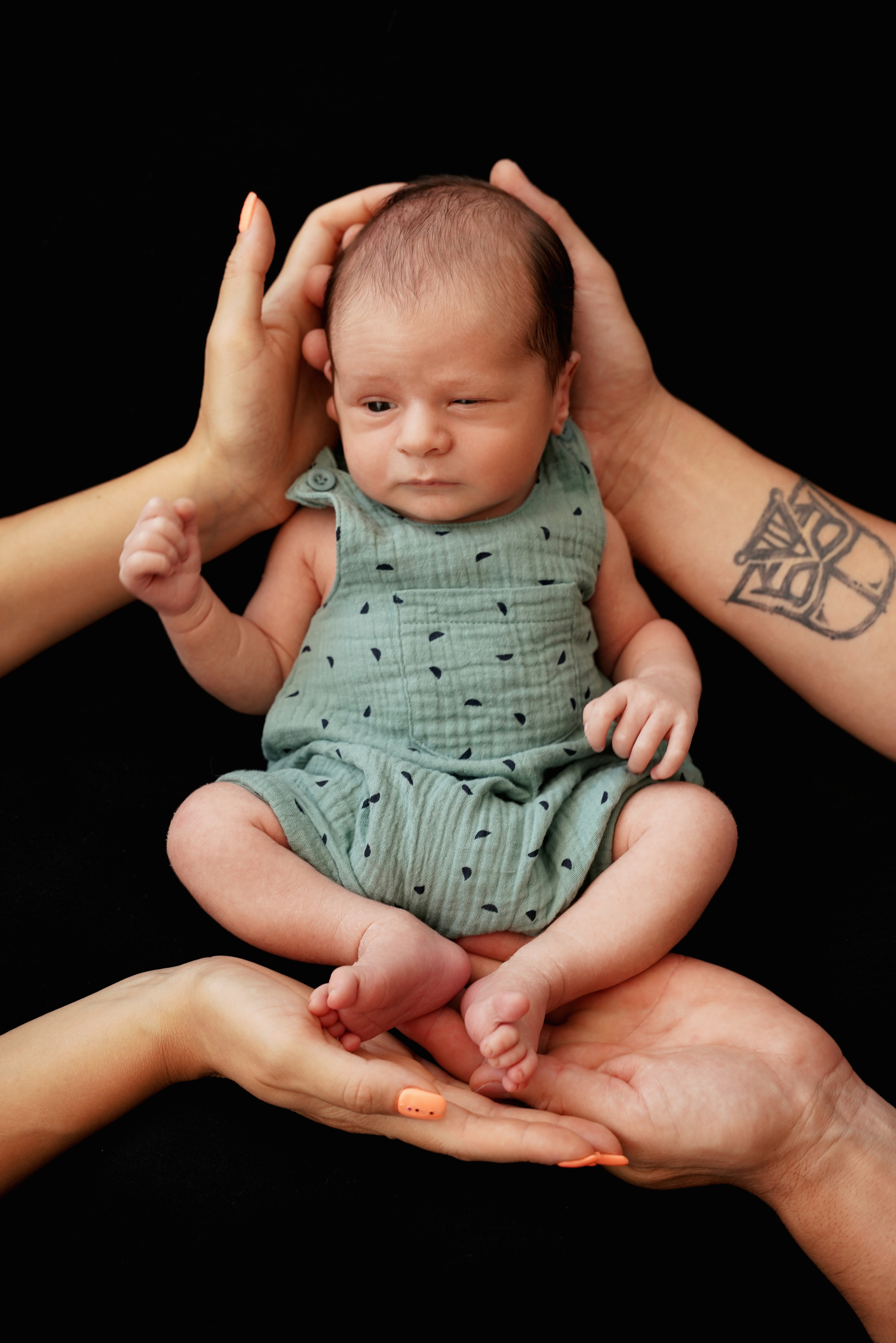 Neugeborenenfotografie eines Jungen auf schwarzem Hintergrund mit den Händen von Eltern