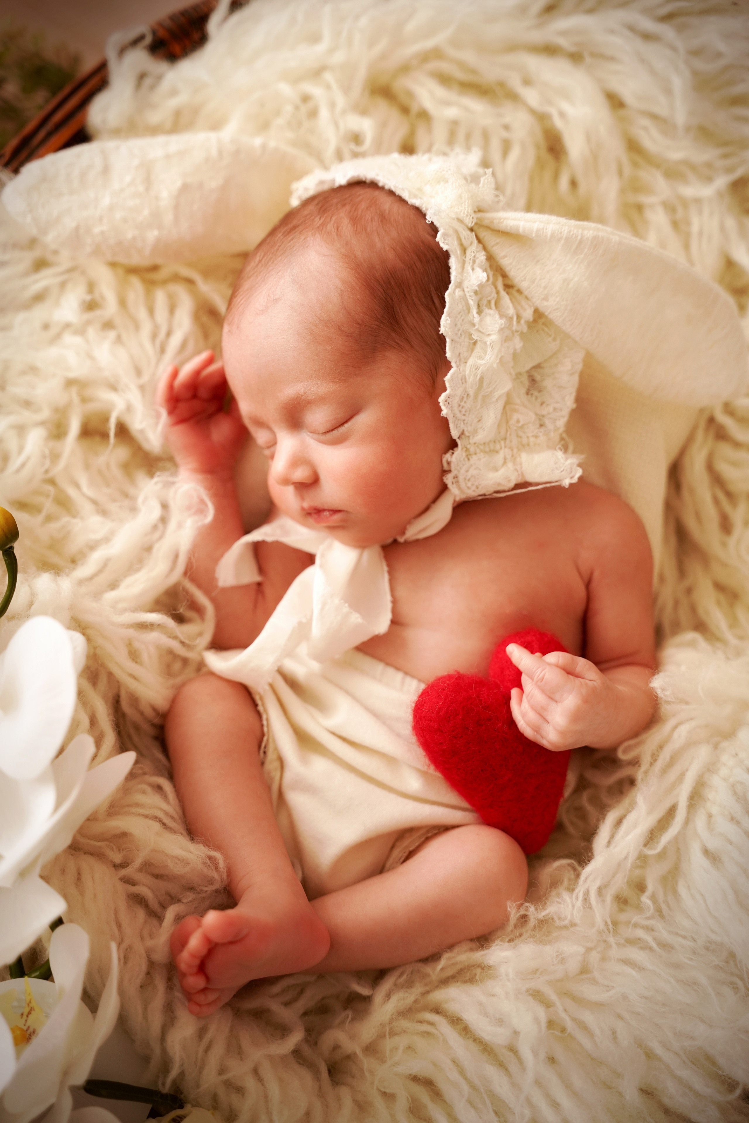 Ein rotes Herz wird von den Fingern eines neugeborenen Mädchens gedrückt