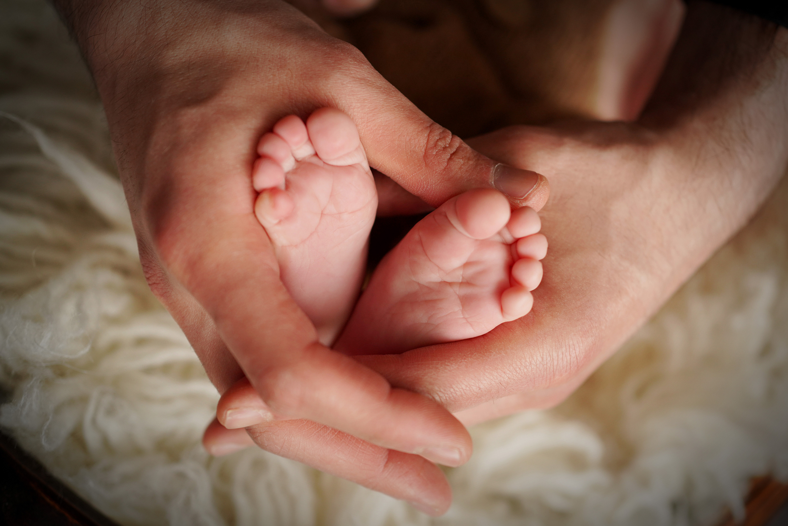 Babys Fersen in einem Herzen aus Papas Händen