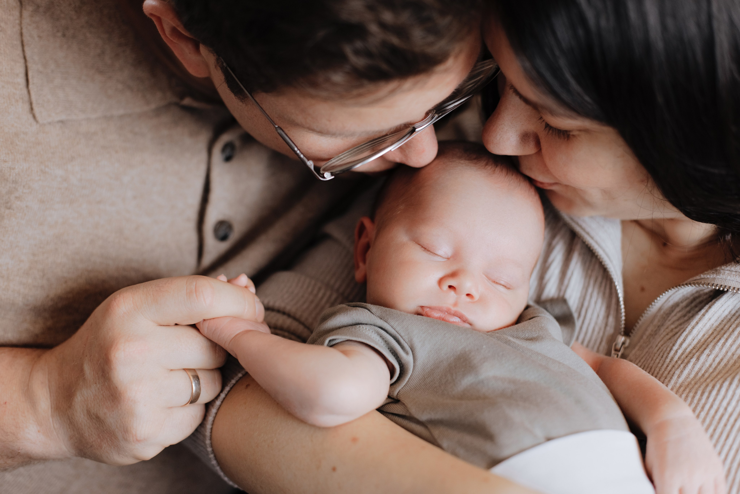 Mama und Papa küssen ihren neugeborenen Sohn liebevoll auf die Stirn während eines Neugeborenen-Fotoshootings.