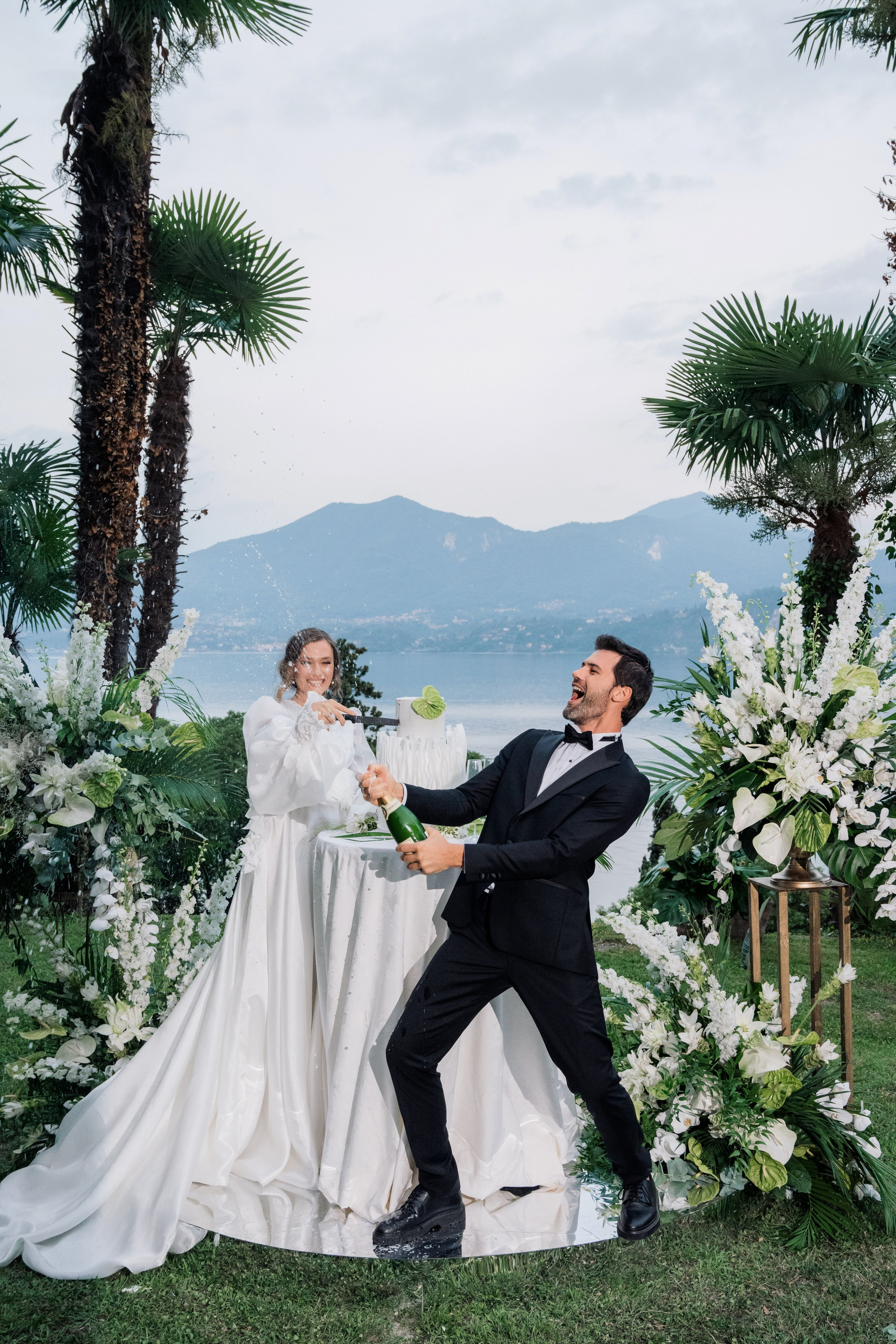 a bride and groom are sitting on a wooden bench with flowers and greene