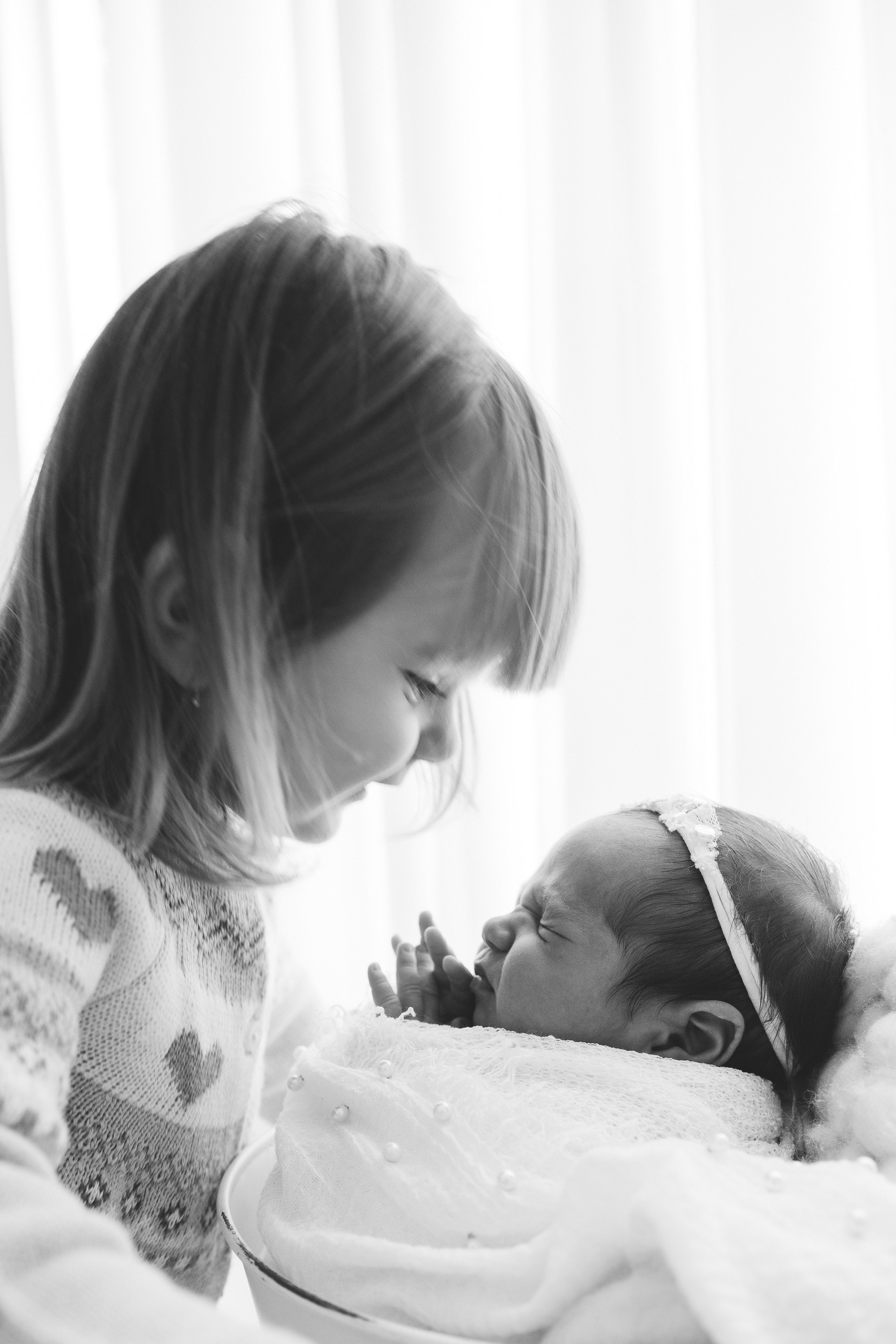 irmã mais velha observando bebê recém-nascido em ensaio em Sorocaba