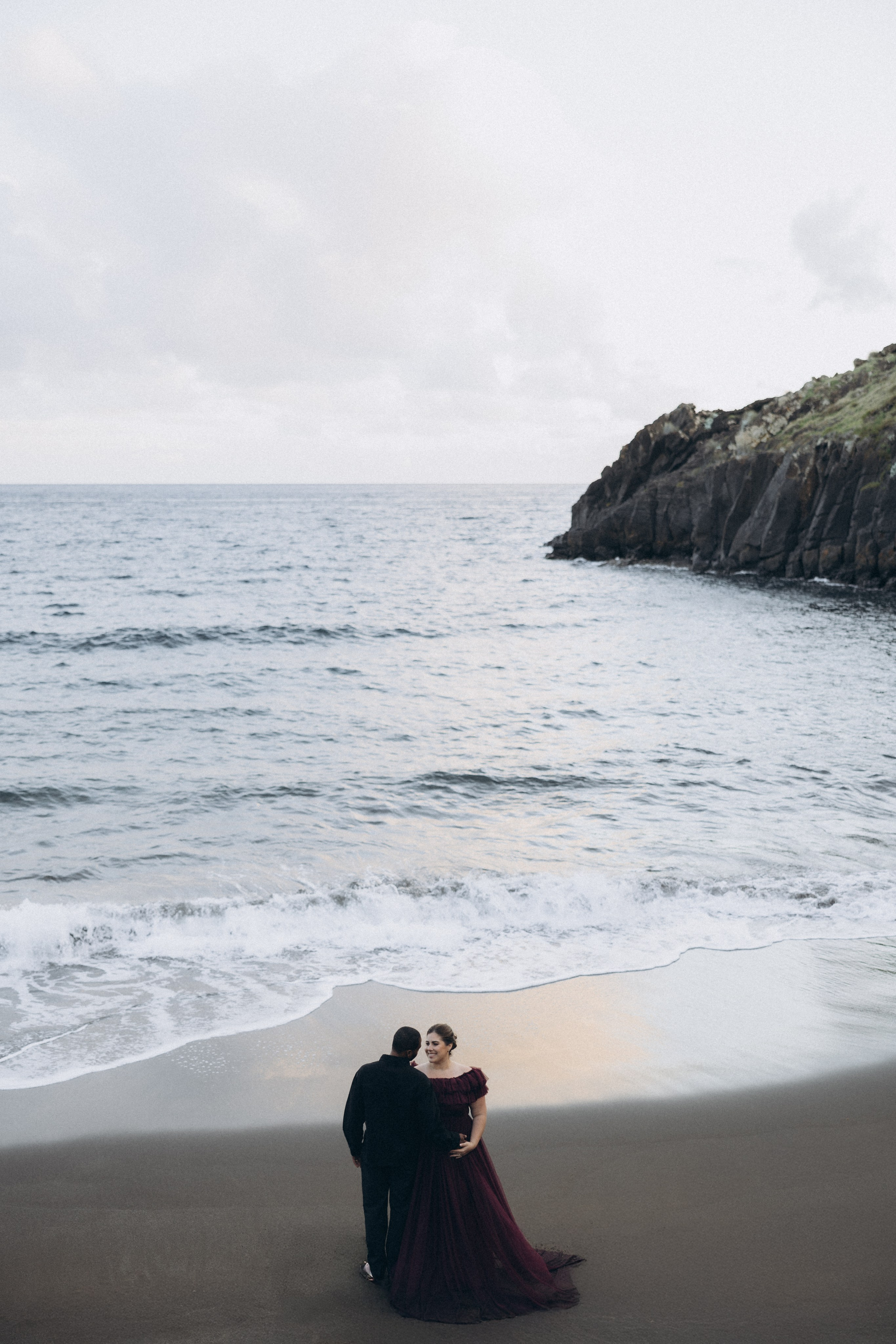 A glowing expectant mother standing on a cliff overlooking the ocean in Madeira, her dress flowing gently in the wind as the golden sunset casts a warm glow.