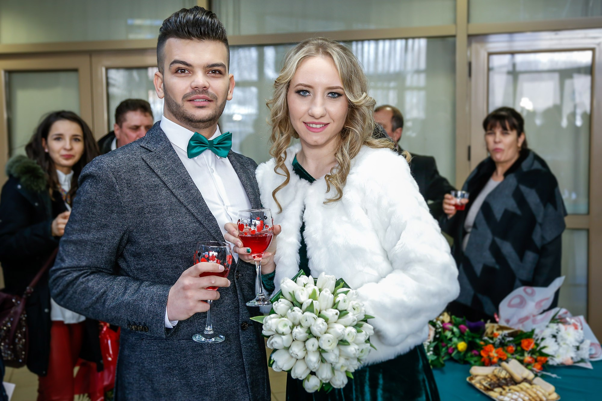 Smiling bride and groom toasting with champagne glasses alongside their guests at the end of a joyful civil ceremony.