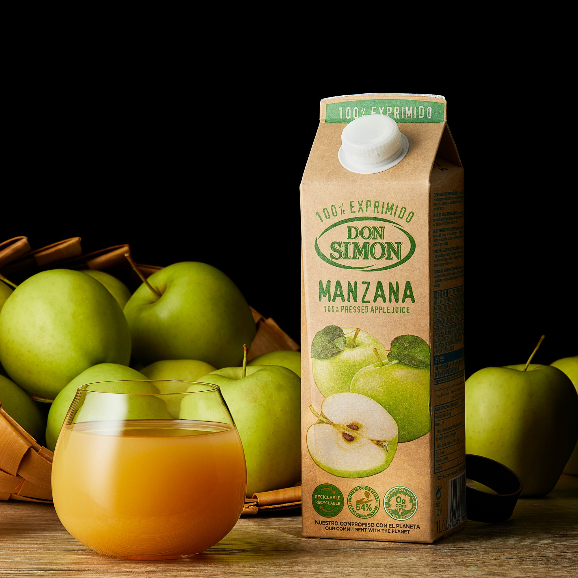 Photographer Roman Djuzev - The photograph shows Don Simon brand apple juice poured into a transparent glass, with a juice carton placed next to it. Behind the glass and the carton, part of a basket with apples is visible, and the background is dark.