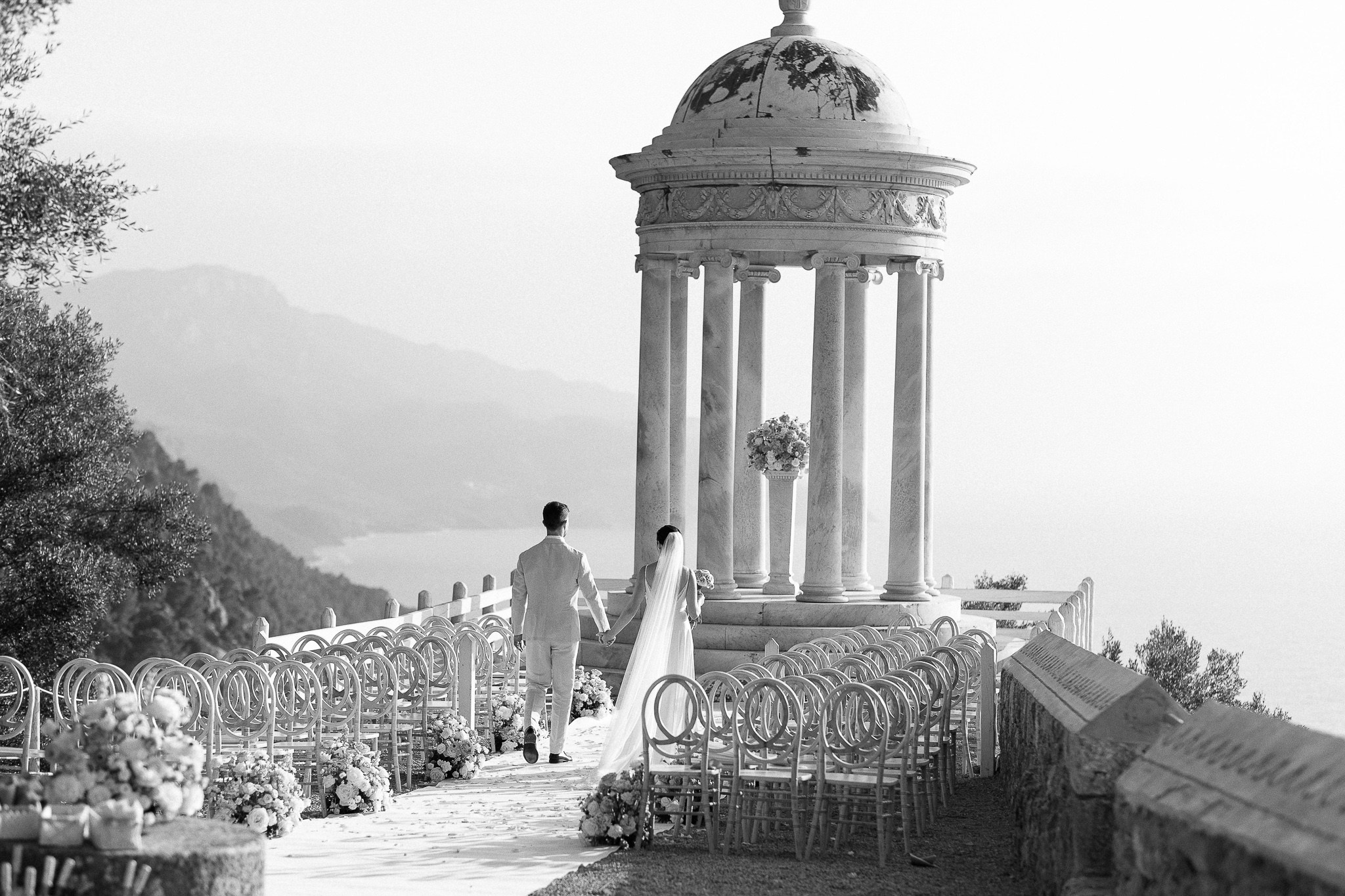 Bride and groom walking hand in hand toward the Son Marroig temple at sunset, Mallorca wedding ceremony with sea view