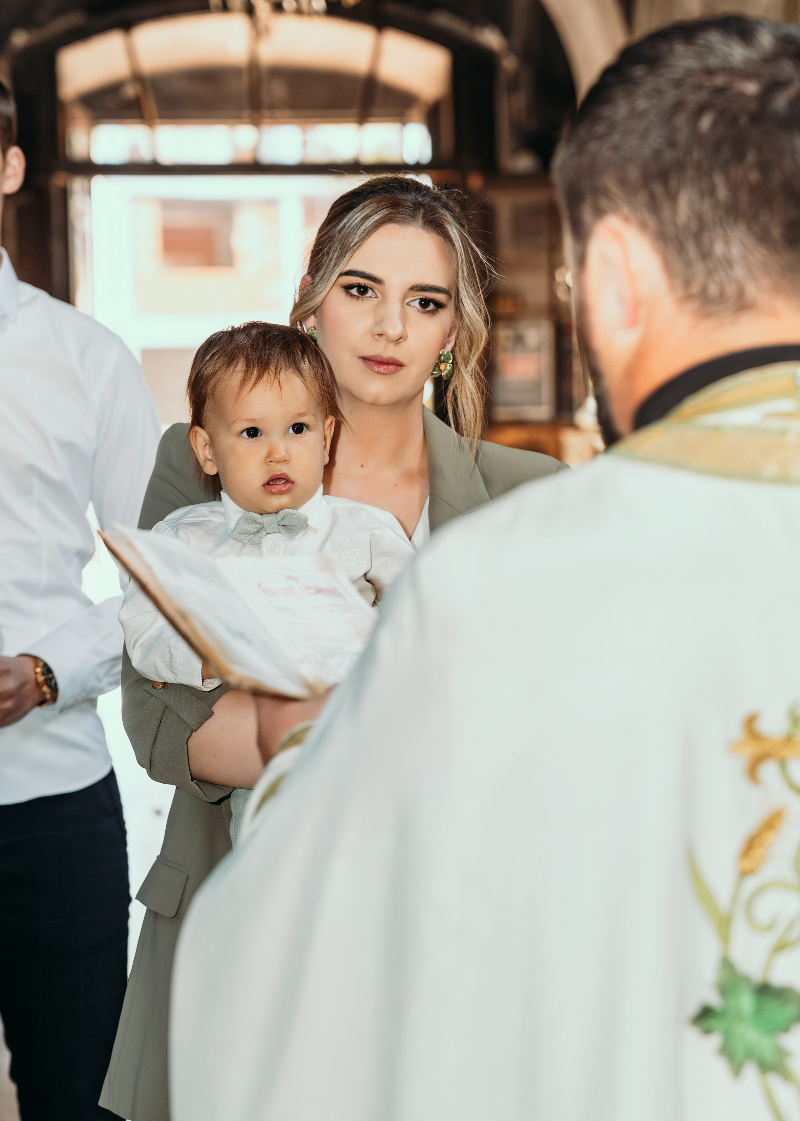 Kuma drzi decaka u beloj kosulji na krstenju