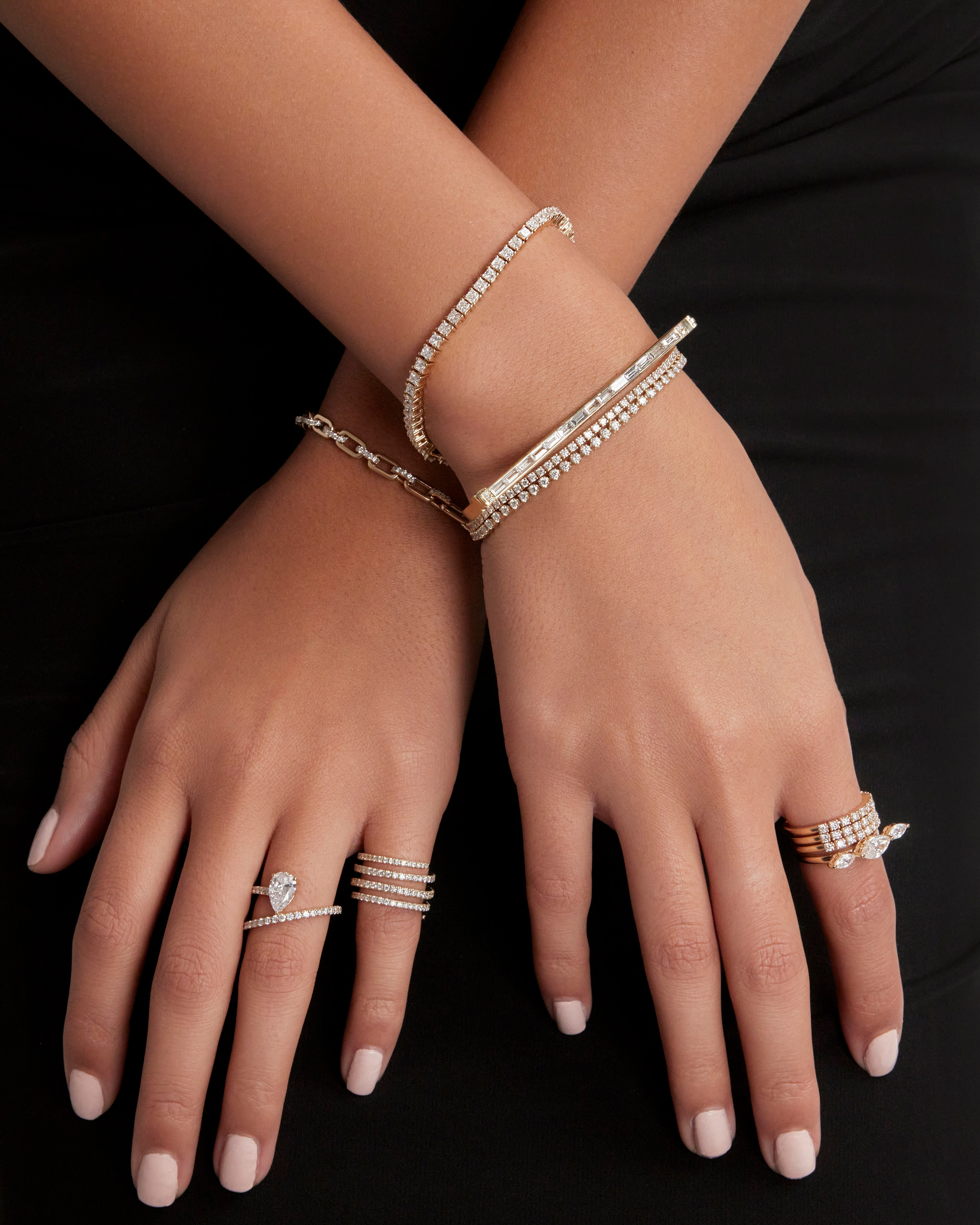 Close-up of hands wearing gold jewelry against a neutral background, highlighting fine craftsmanship.