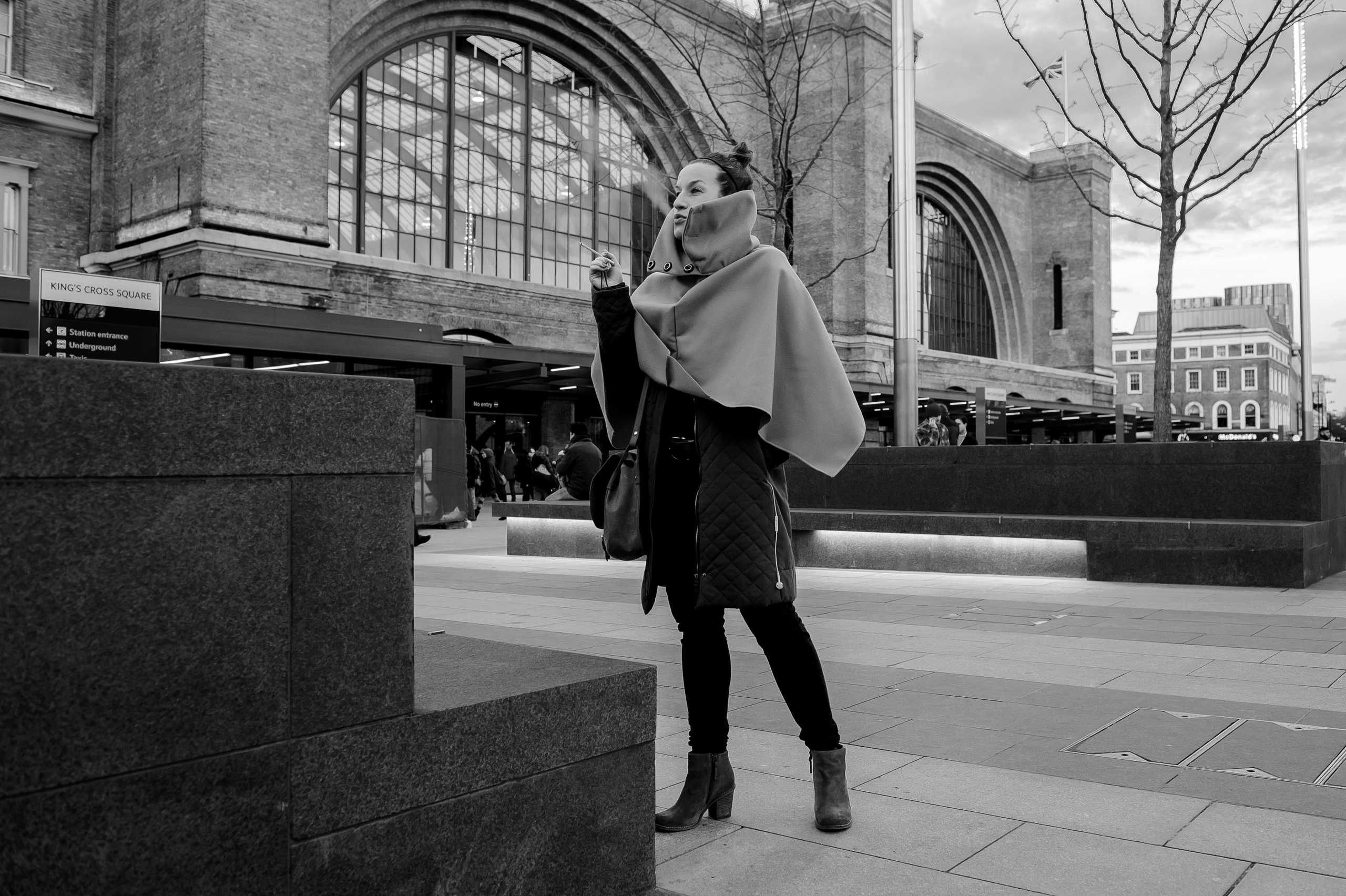 Full-length portrait of a woman against the background of a building with arches.