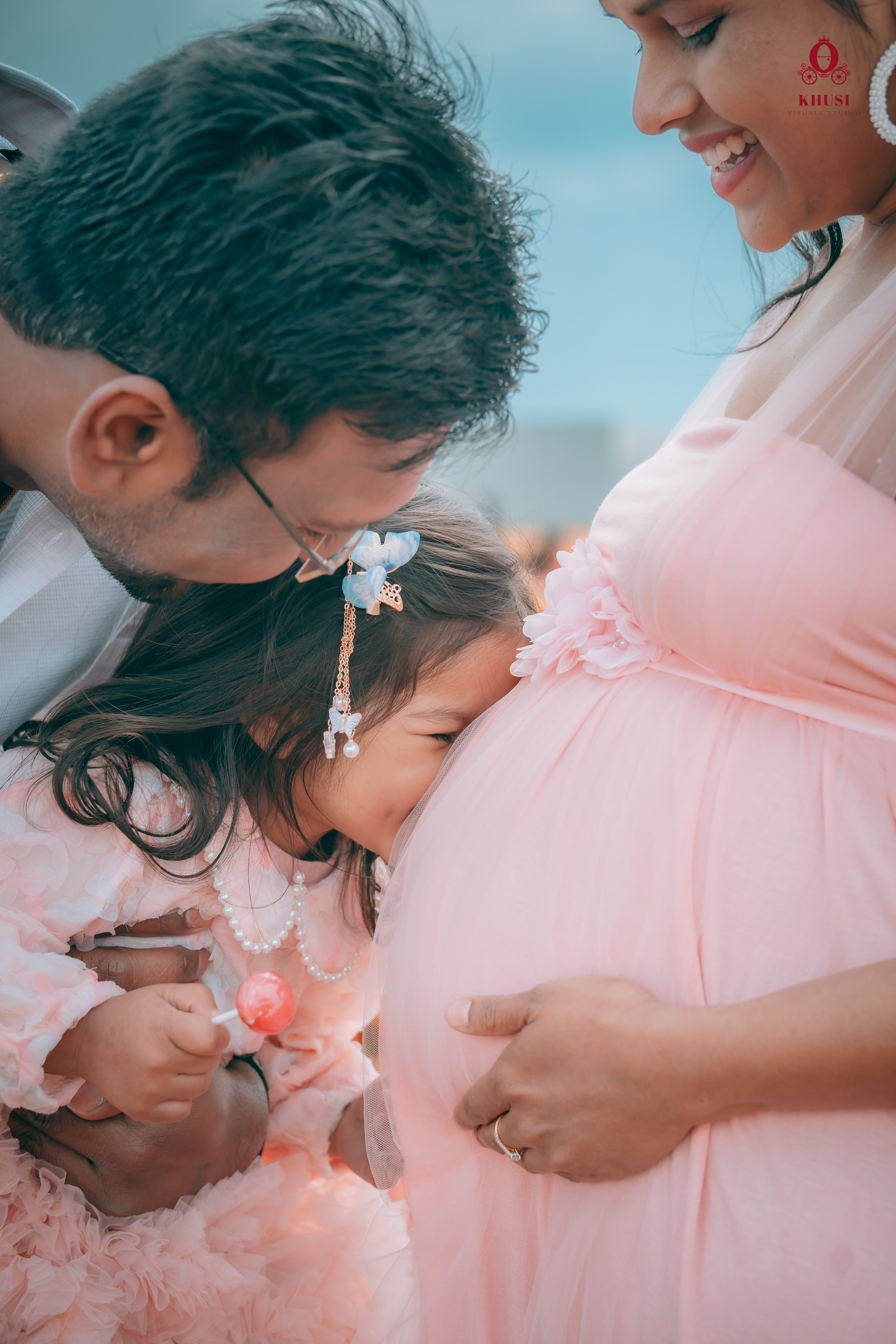 A daughter kissing the baby bump of a pregnant woman and her husband is holding their daughter in a tulip fields