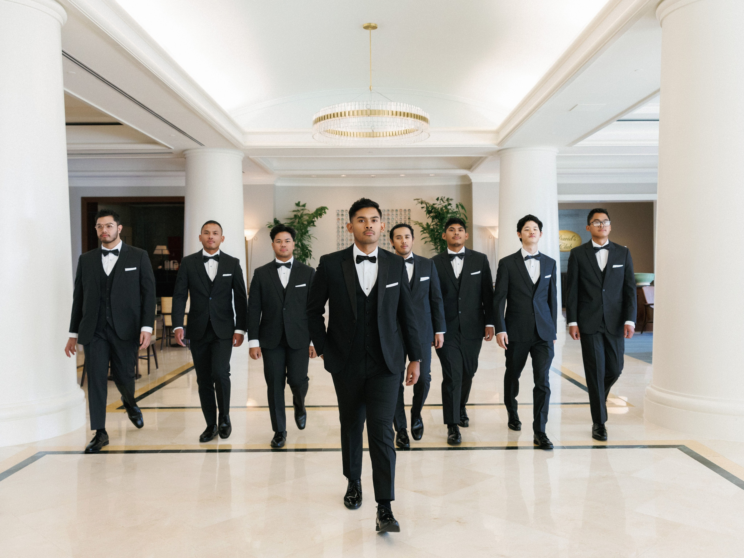 Groom walking with his groomsmen through a grand indoor hallway