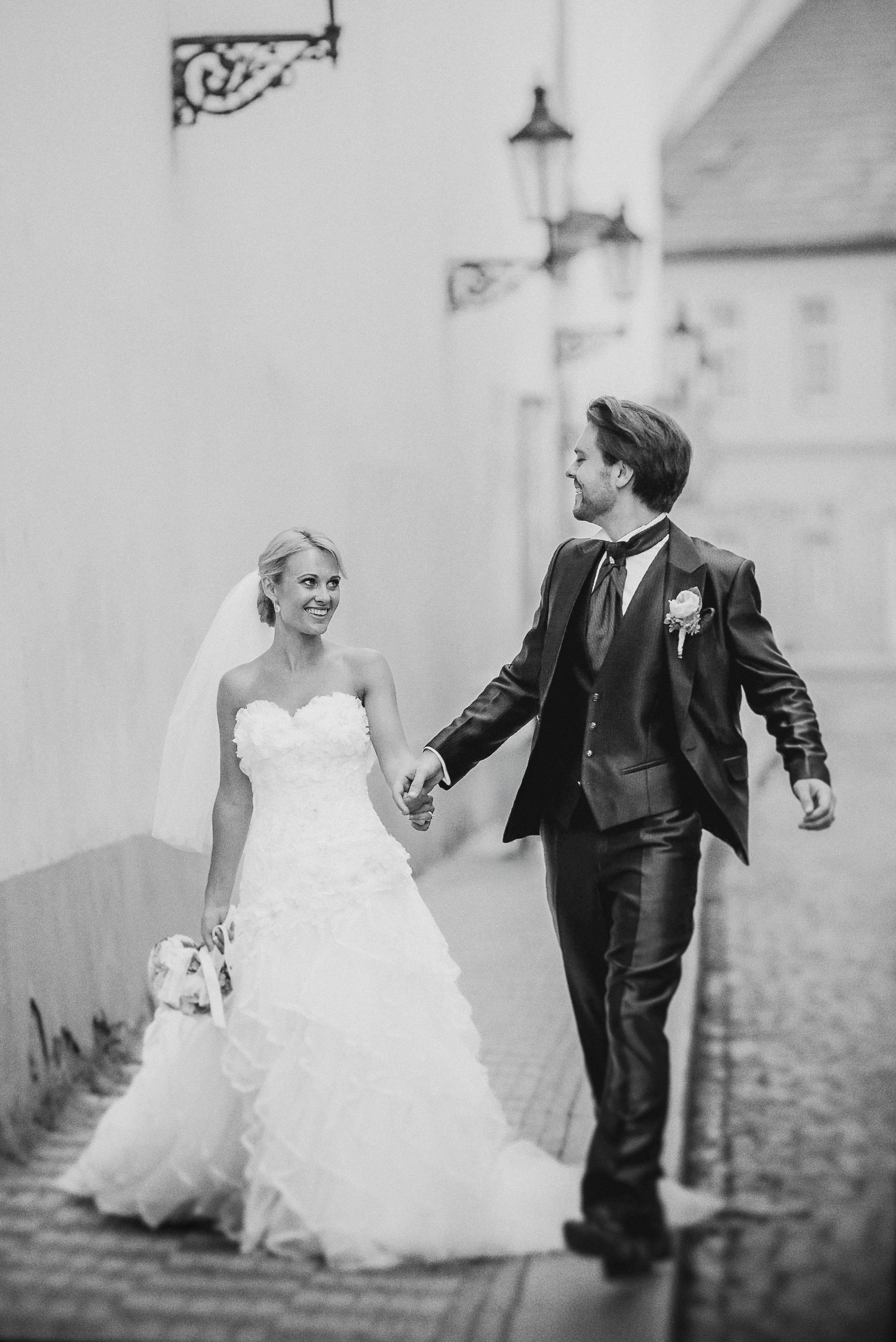 A smiling bride looks towards her groom as they walk through Prague's historical Mala Strana quarter.