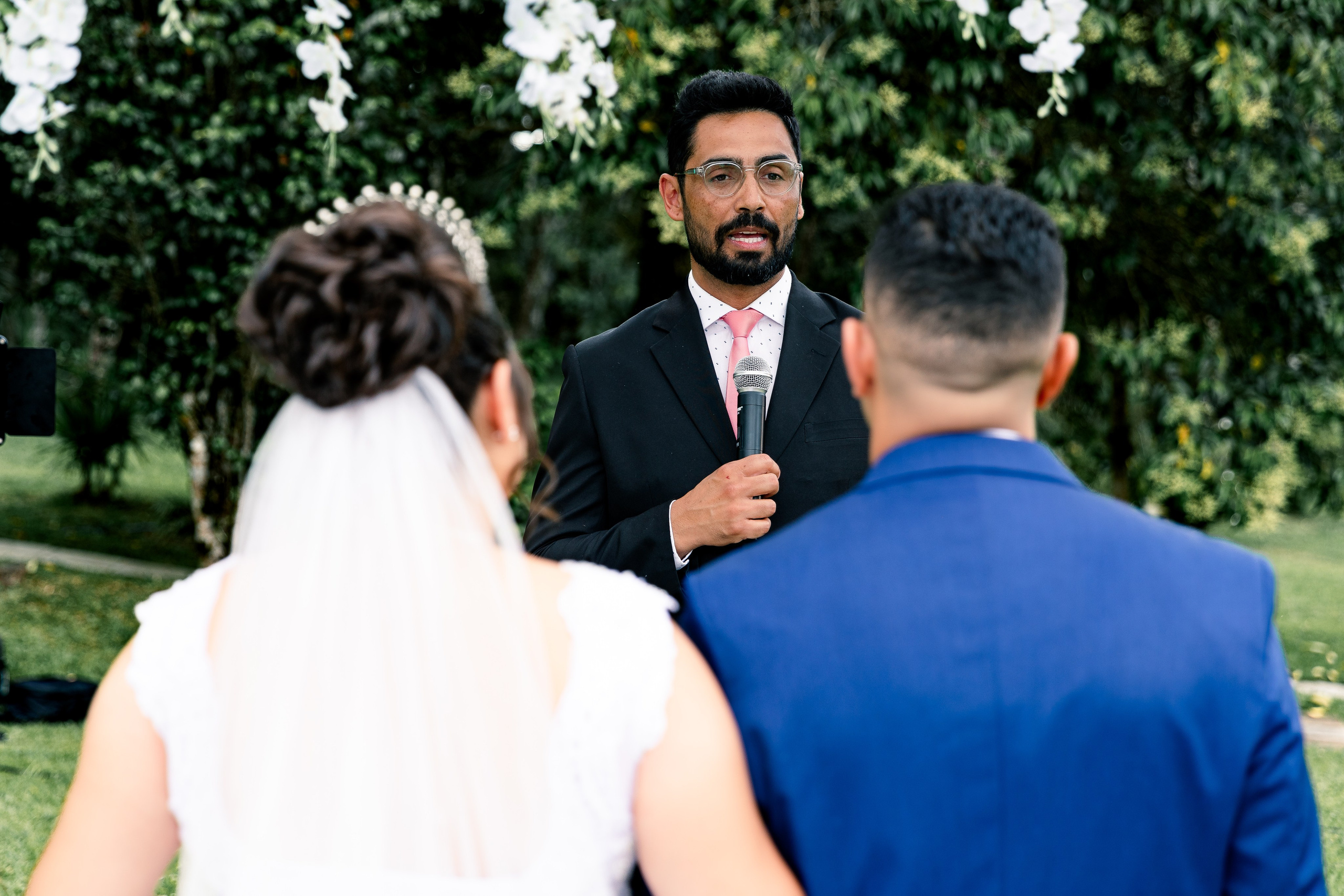 Celebrante conduzindo a cerimônia com leitura de votos no altar decorado com flores brancas.
