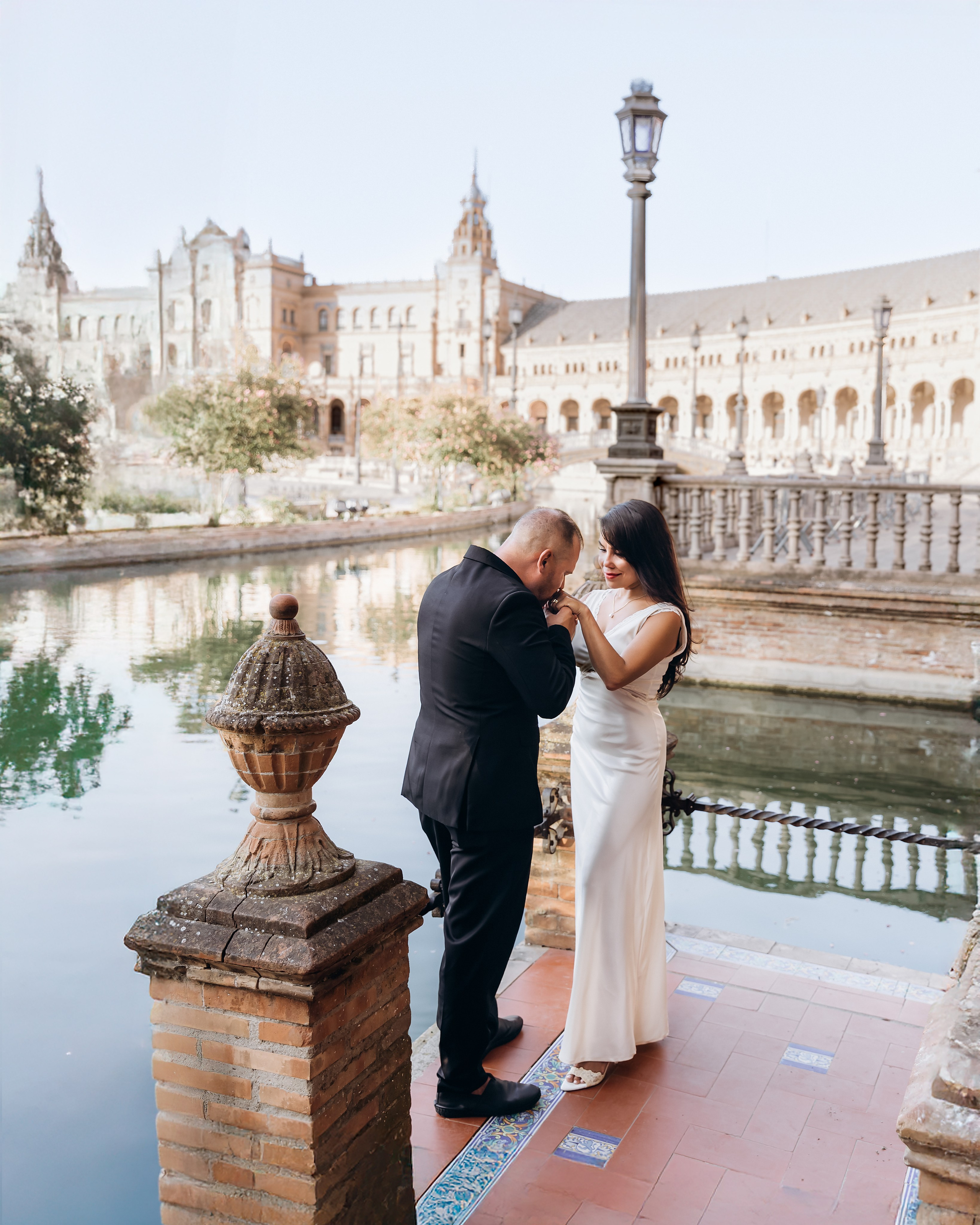 Bride and groom sharing a quiet embrace beside the canal at Plaza de España in Sevilla. Romantic sunset scene from their small civil wedding in Spain.