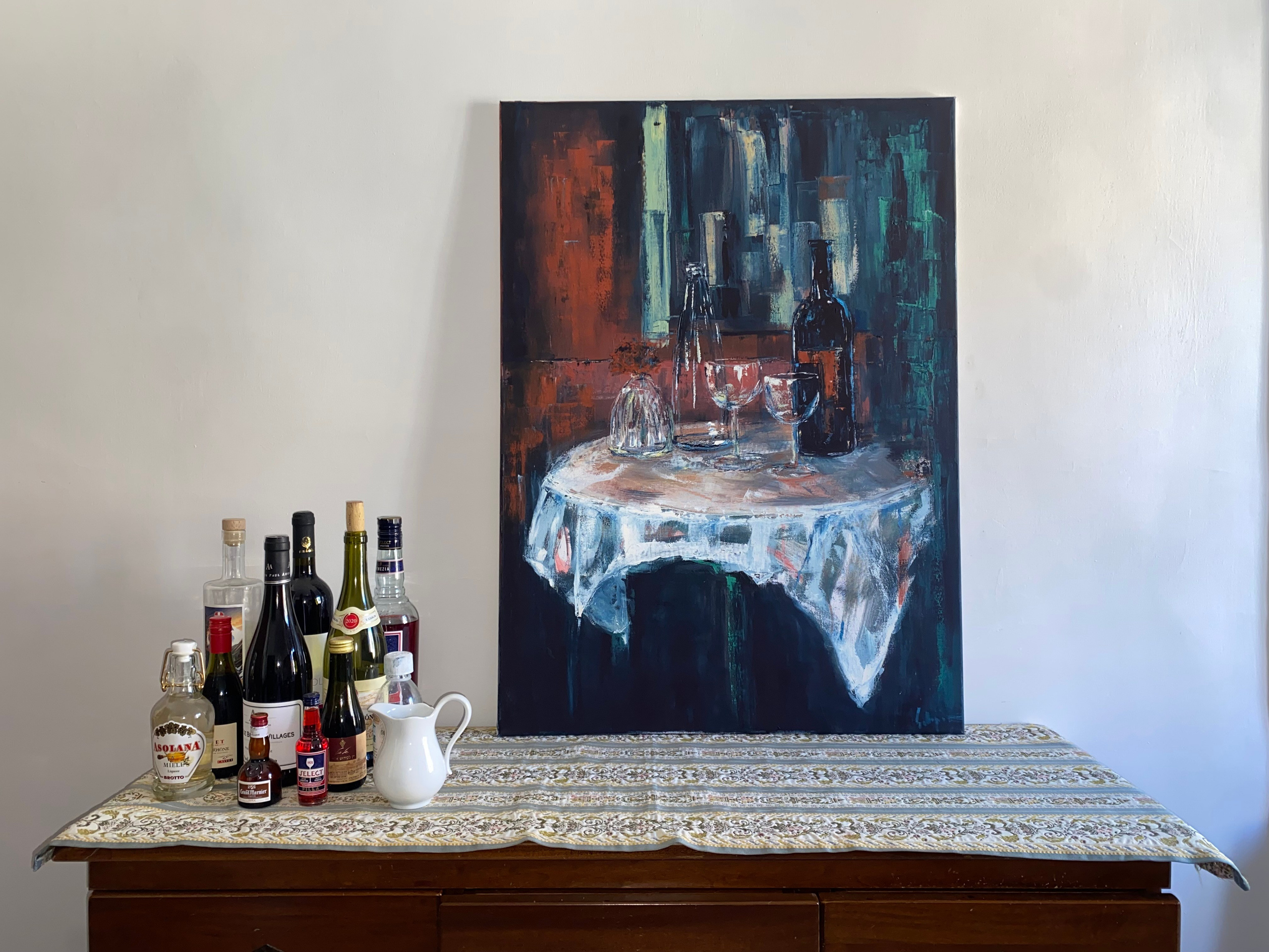 Expressive acrylic still life of a bar table with bottles, wine glasses, and a patterned tablecloth, rendered in warm reds and deep greens. Painting by Ekaterina Solopova addressing rituals of drinking and shared moments in bars restaurants and aperitivo time.