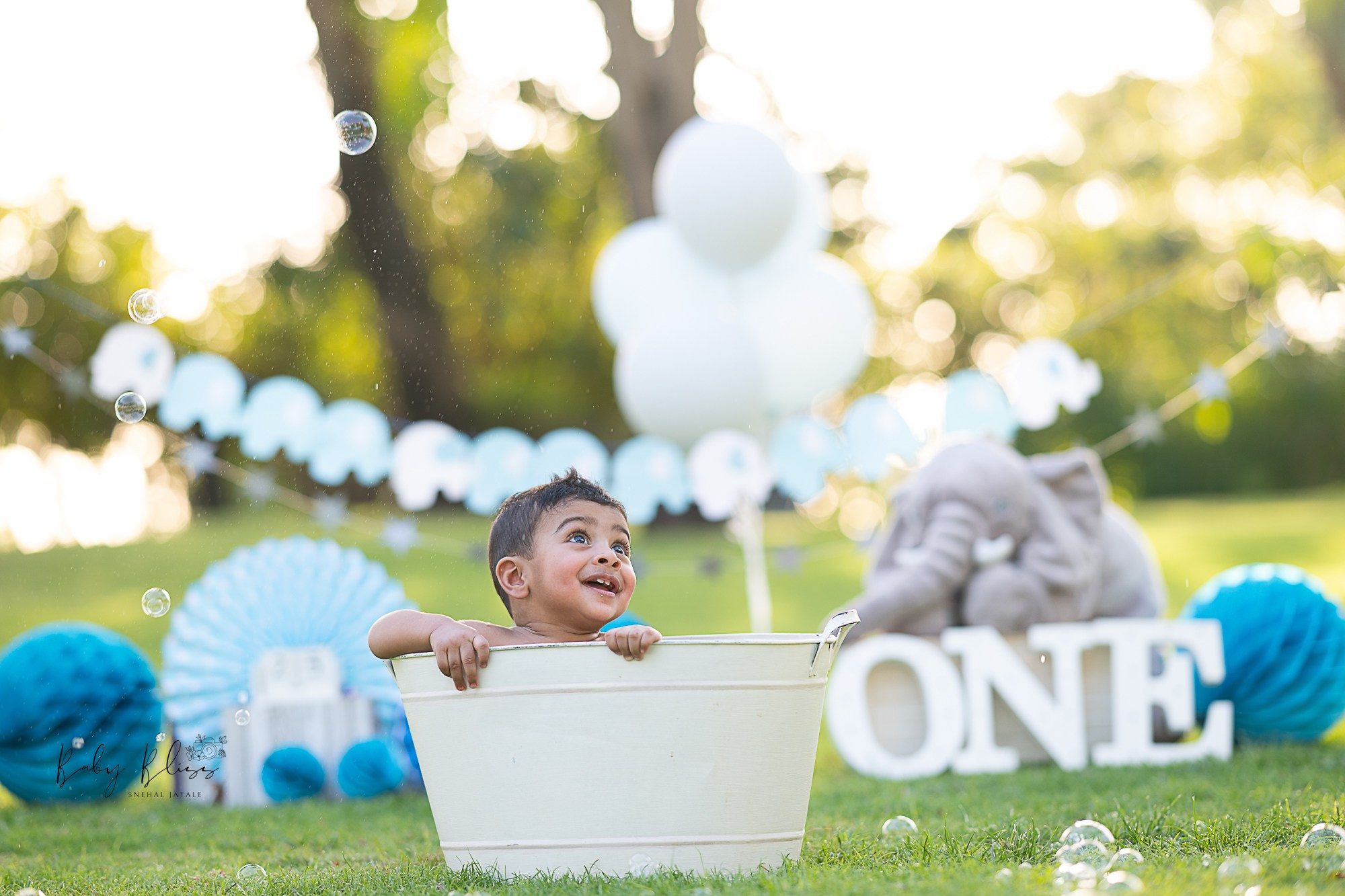 baby enjoying bubble bath in a green park with blue themed background decoration in Doha