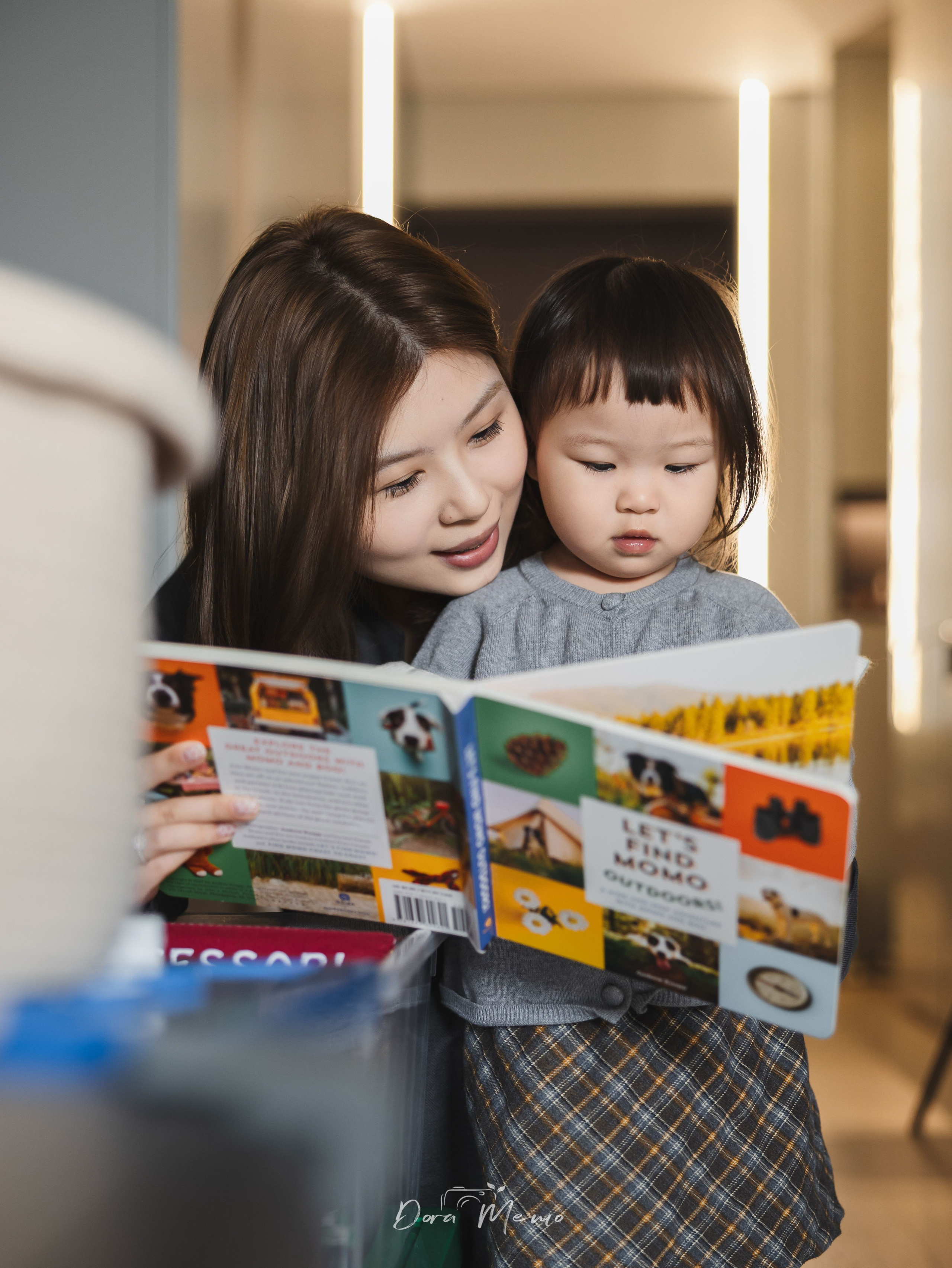Mother holding her daughter while reading a picture book together on the sofa, intimate family moment in their Shanghai apartment.