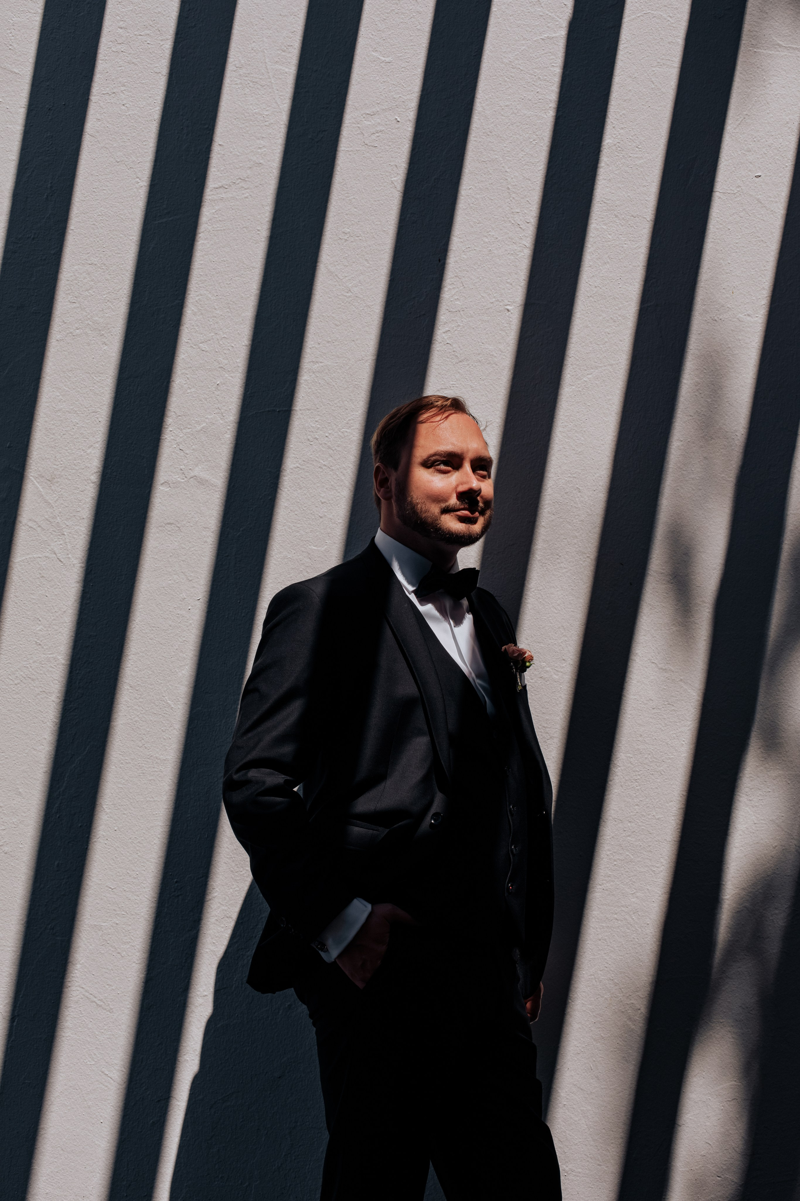 Der Bräutigam steht vor einer Wand, auf der faszinierende Licht- und Schattenspiele sichtbar sind, was dem Bild eine dramatische Atmosphäre verleiht.