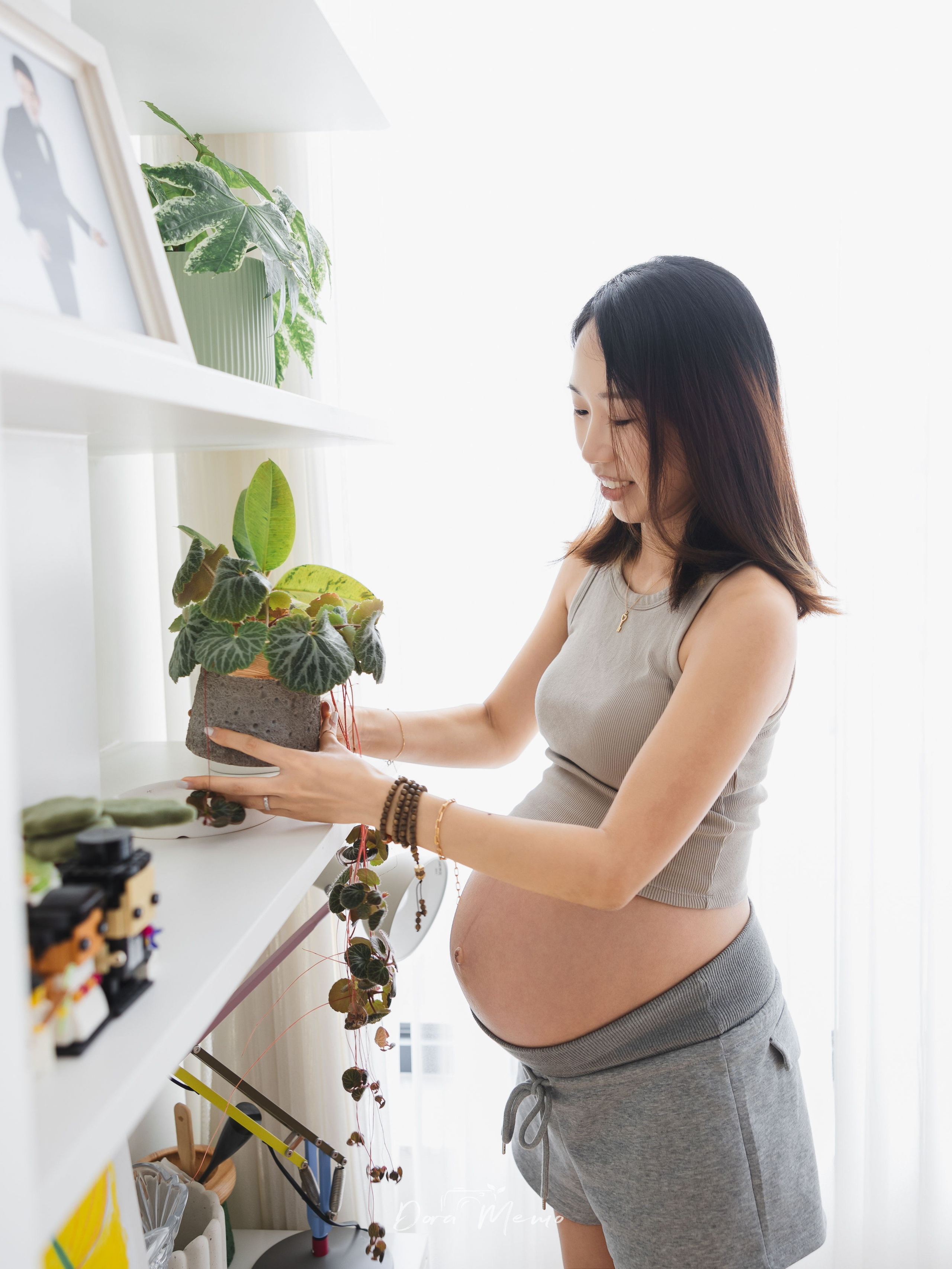 Pregnant mother standing by the window with houseplants in a bright, thoughtfully designed Shanghai home.