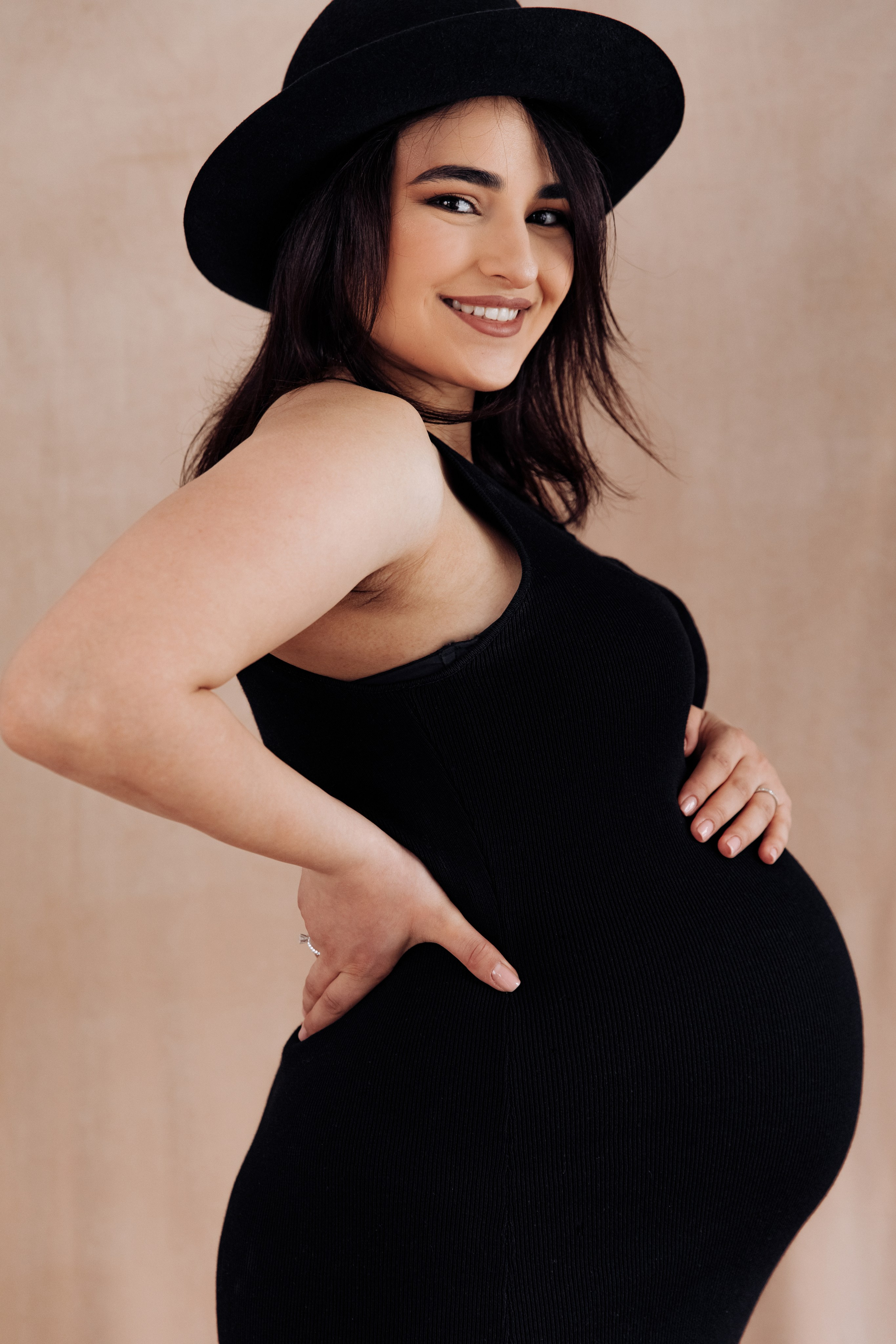 Schwangere Frau mit Hut lächelt glücklich während eines Fotoshootings.