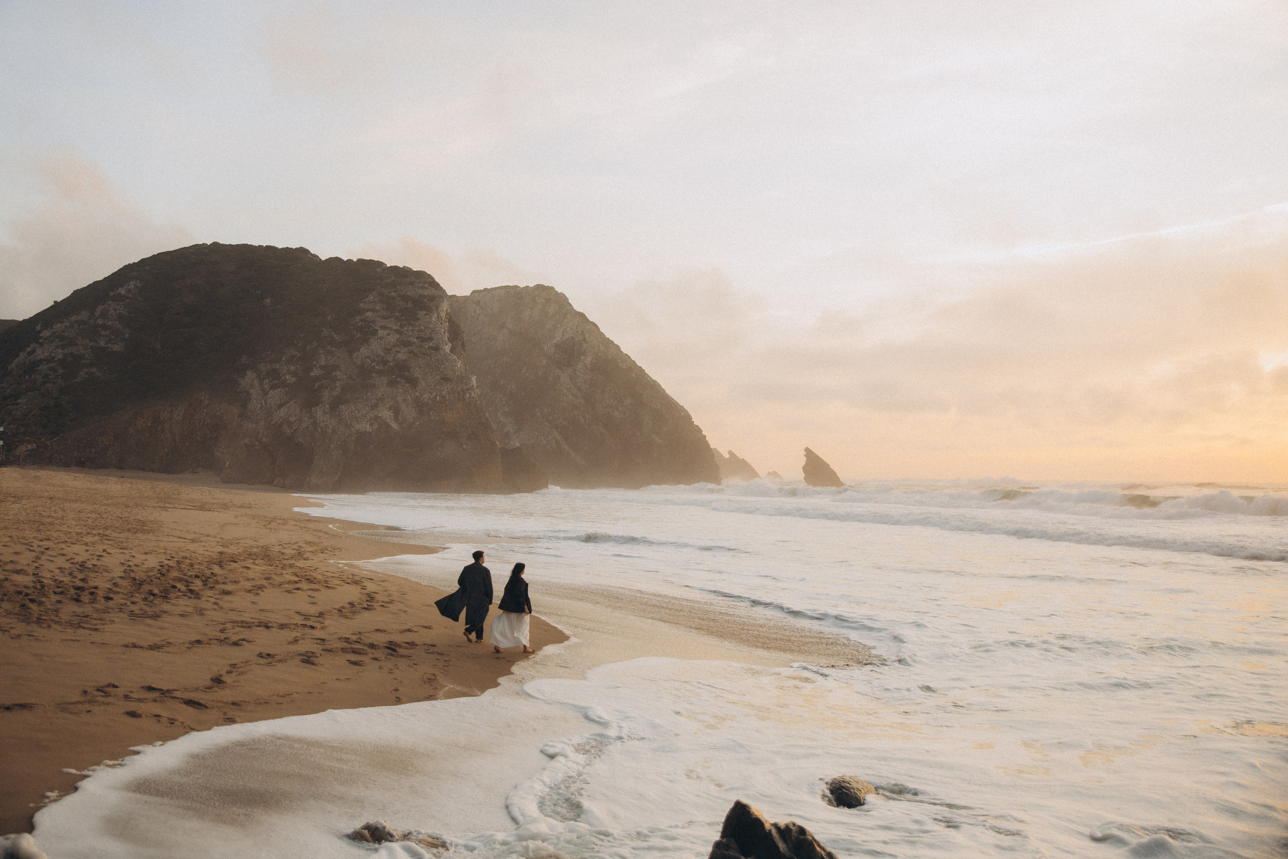 Couple holding hands and walking through a picturesque coastline in Portugal.