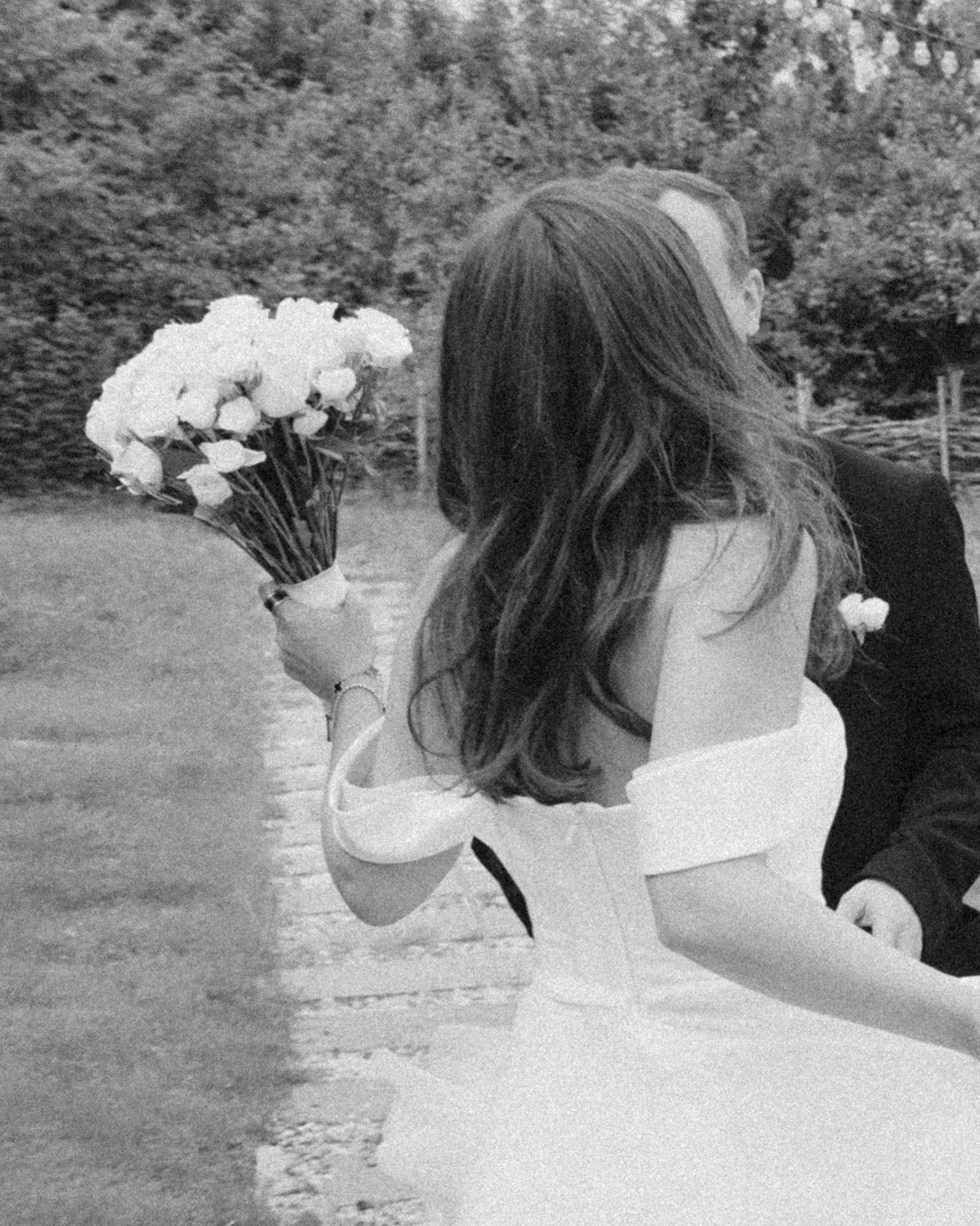 Bride walking away holding flowers in garden