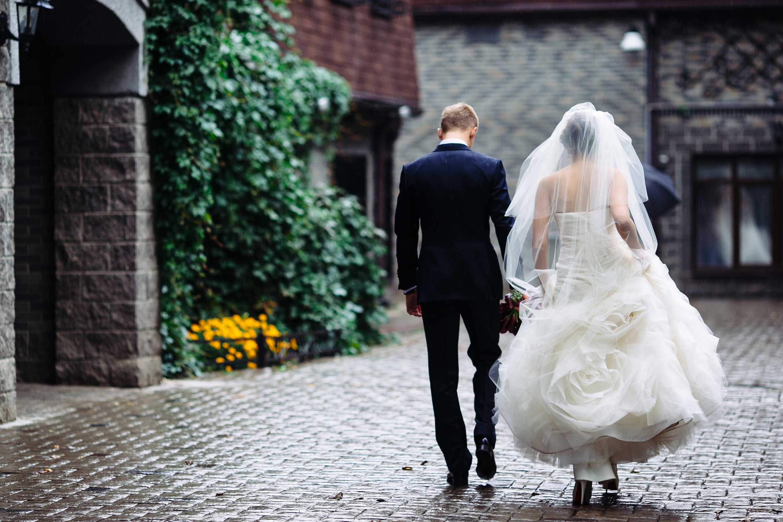 bride wearing the fluffy white dress holding the groom, they are strolling around on the street with green trees on a foreground
