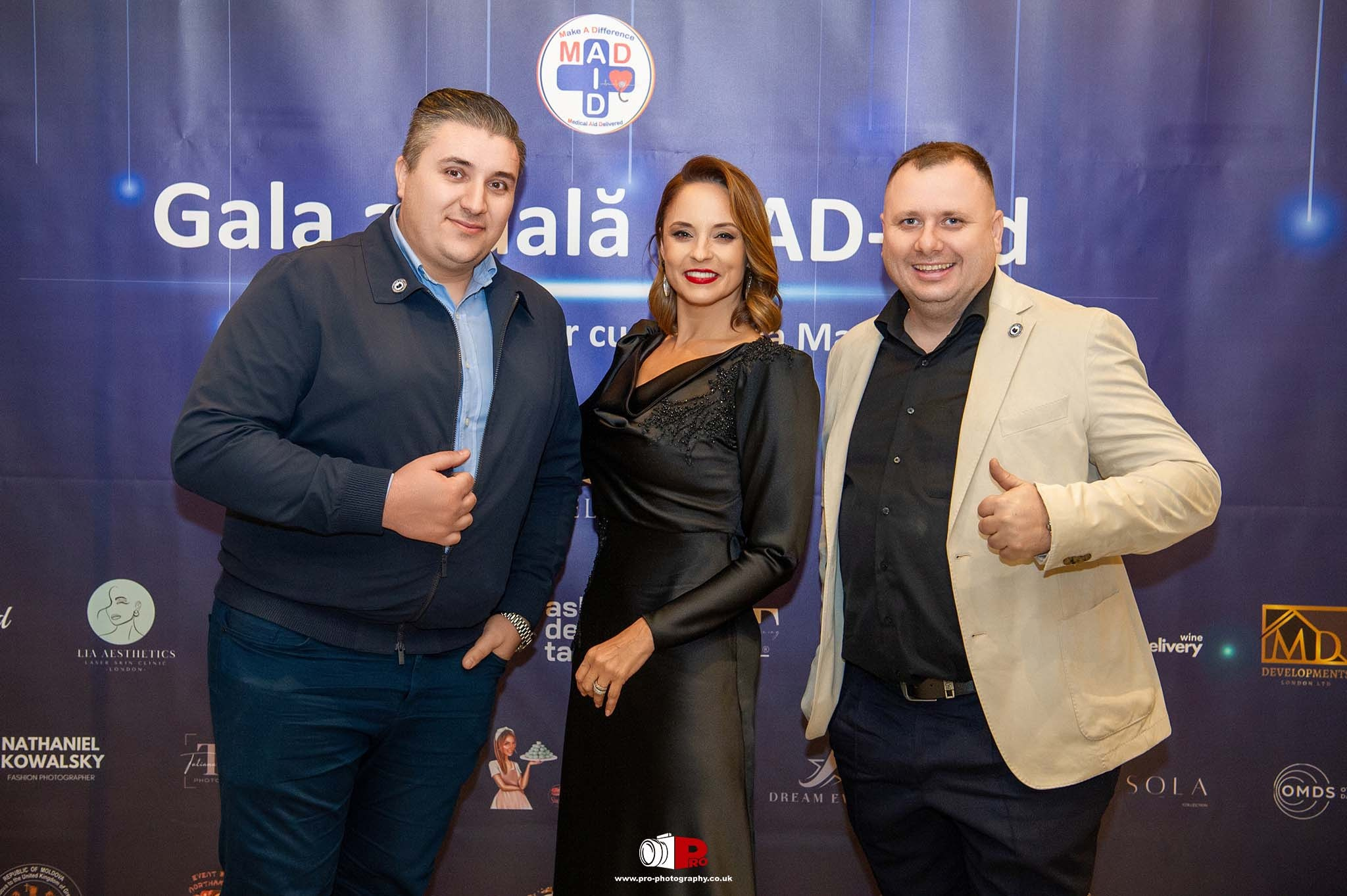 A group photo of key figures at the MAD-Aid Gala posing in front of a blue banner promoting the event.