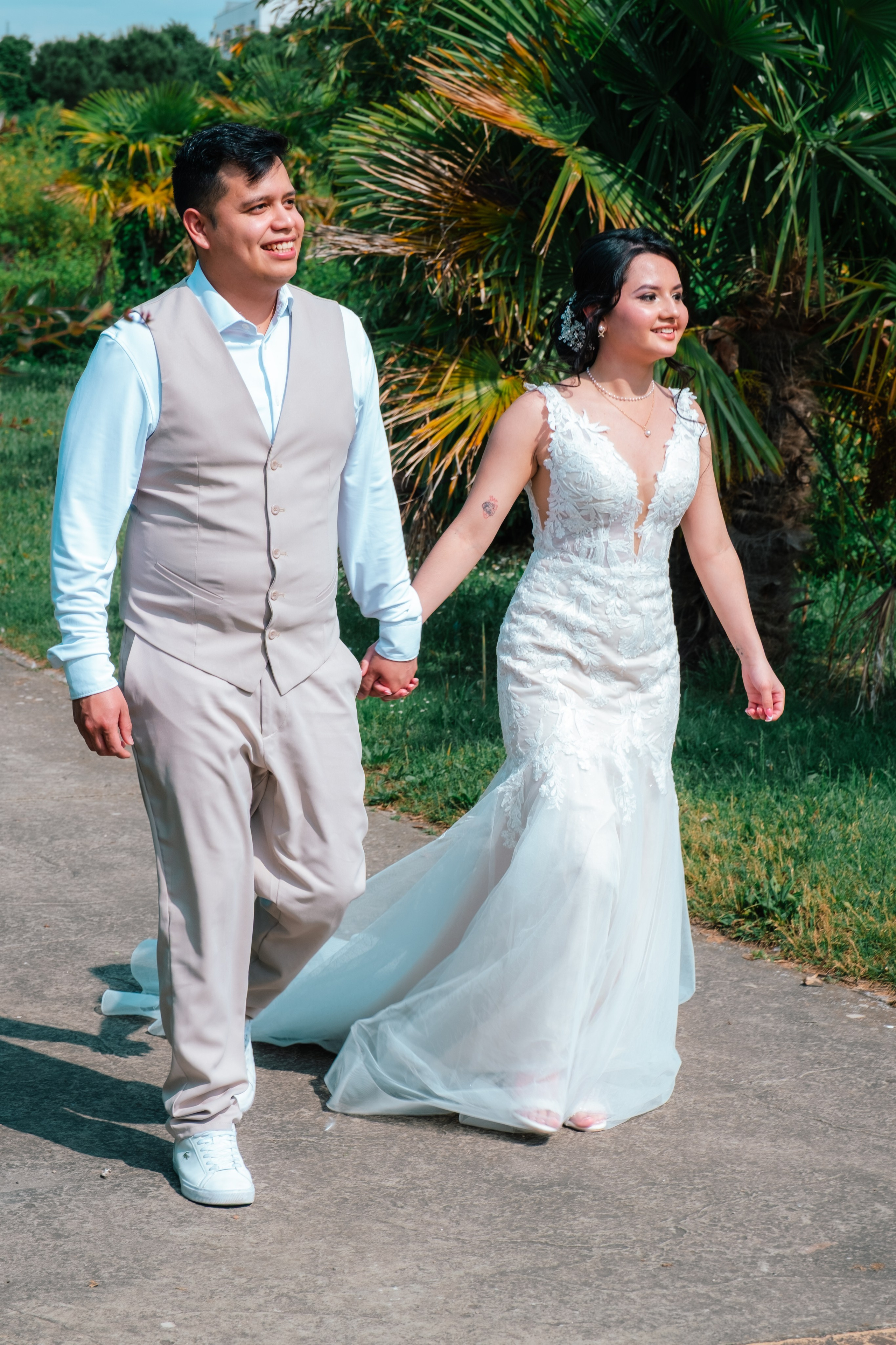 Novios caminando de la mano junto a la vegetación de un jardín