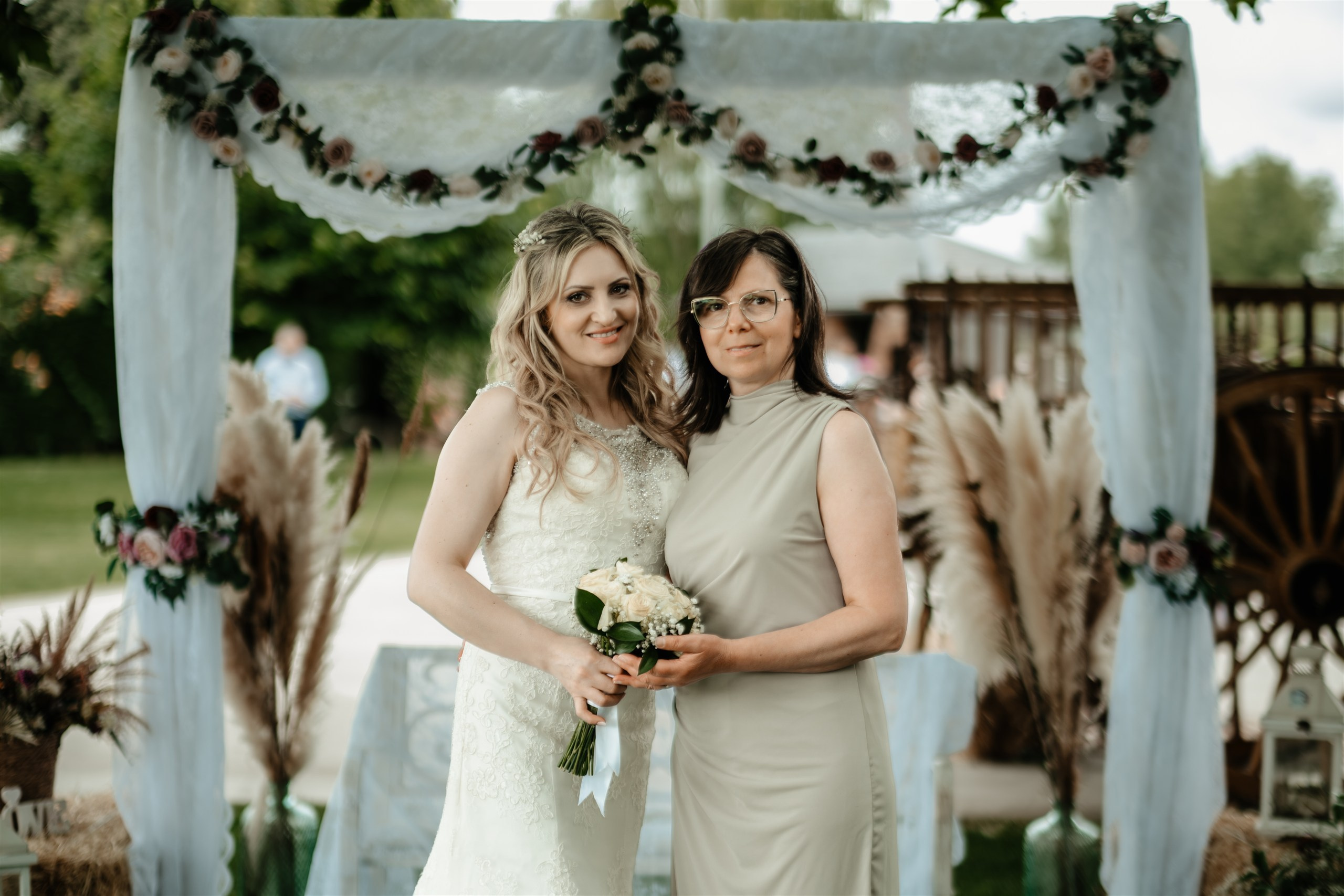 La novia posando con una invitada bajo el arco de flores