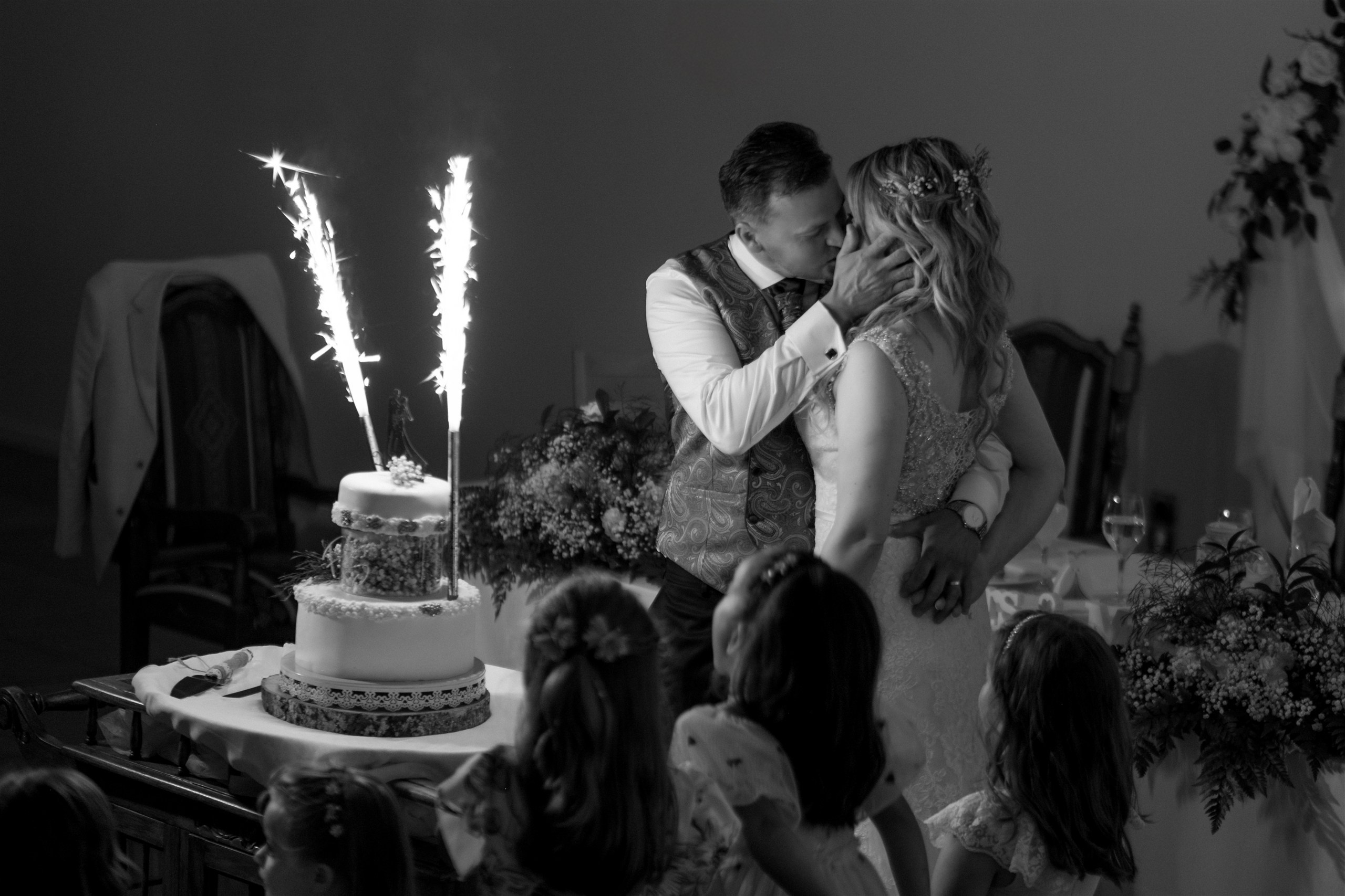 Beso de los novios junto a las bengalas de la tarta, en blanco y negro