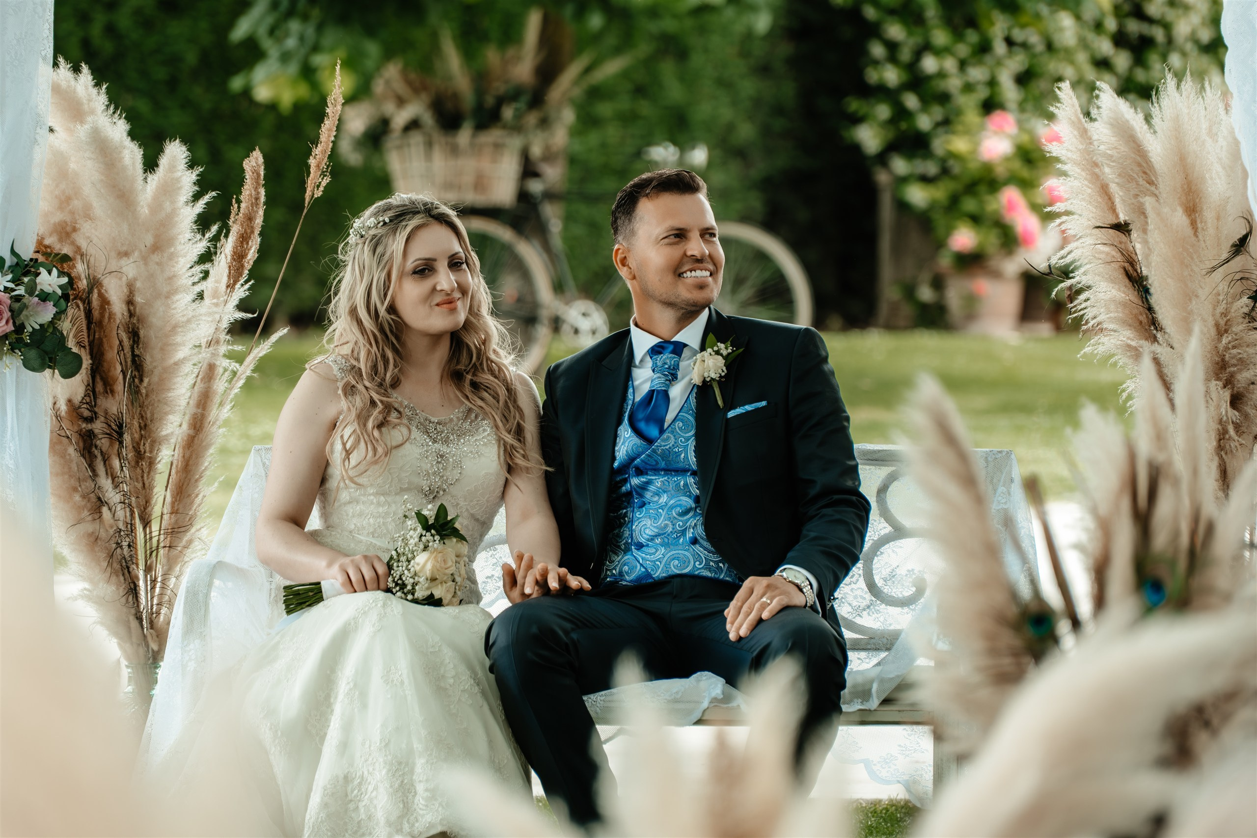 Los novios sentados juntos entre los pampas durante la ceremonia en el jardín