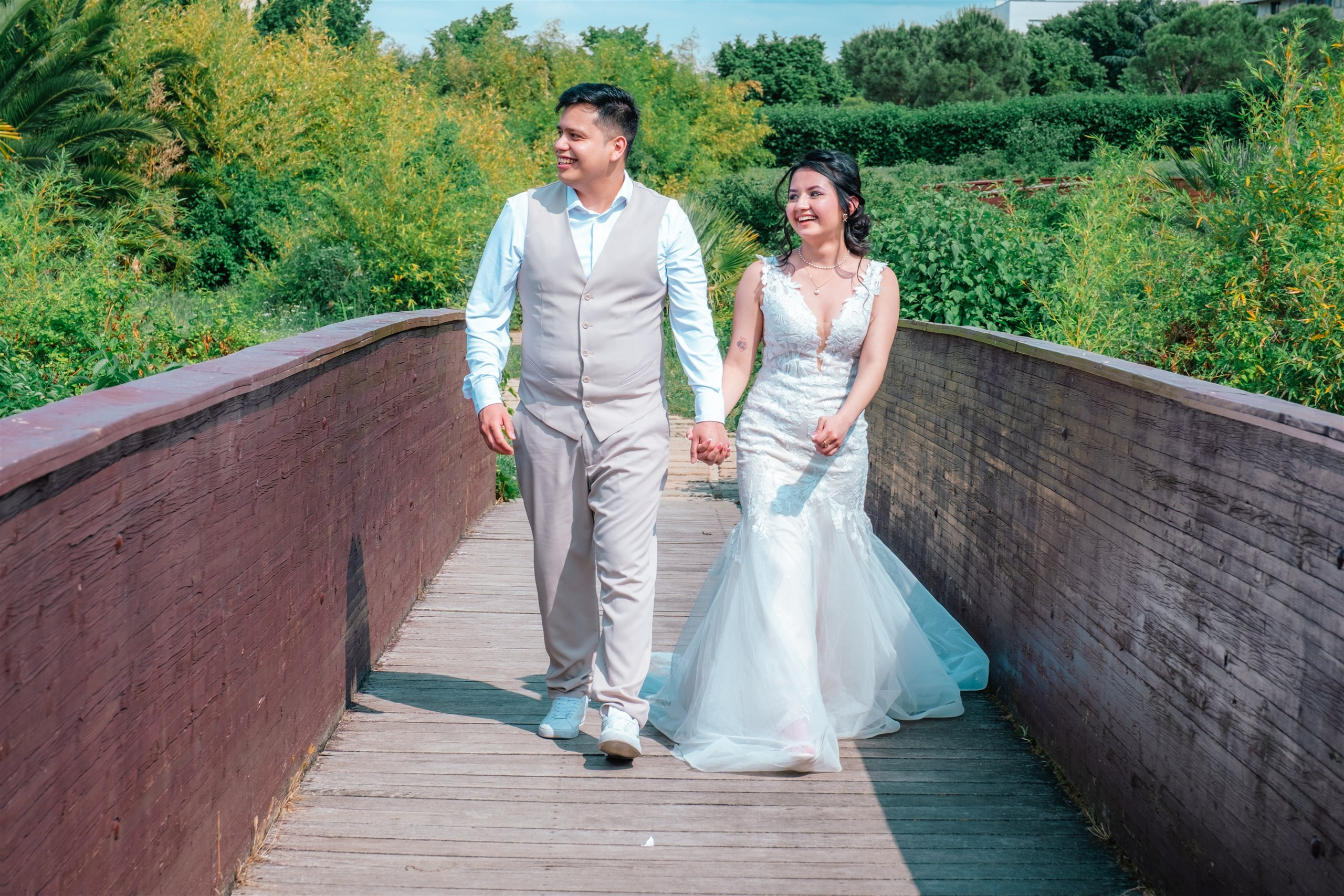 Pareja de novios caminando de la mano por una pasarela de madera en el parque