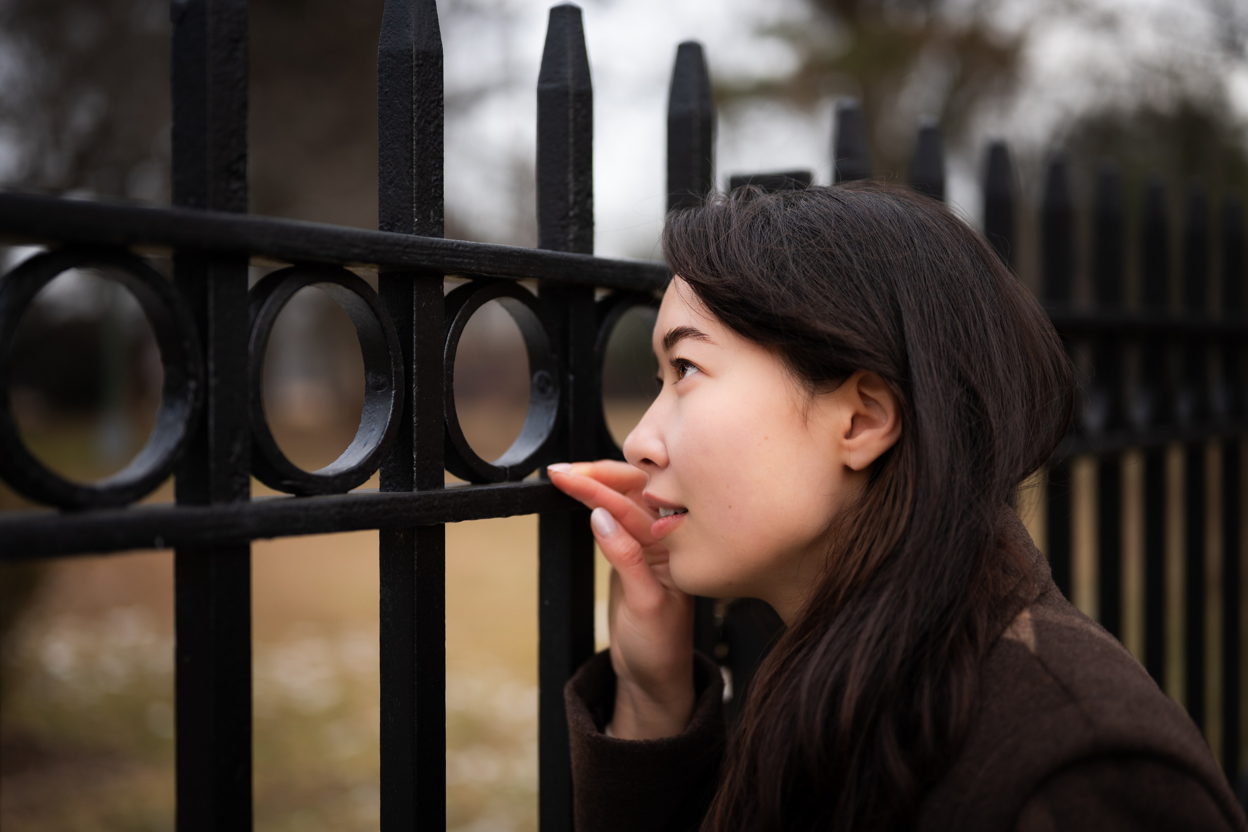 Side profile portrait of a woman by a black iron fence in Van Cortlandt Park, Bronx, New York, winter outdoor photoshoot.