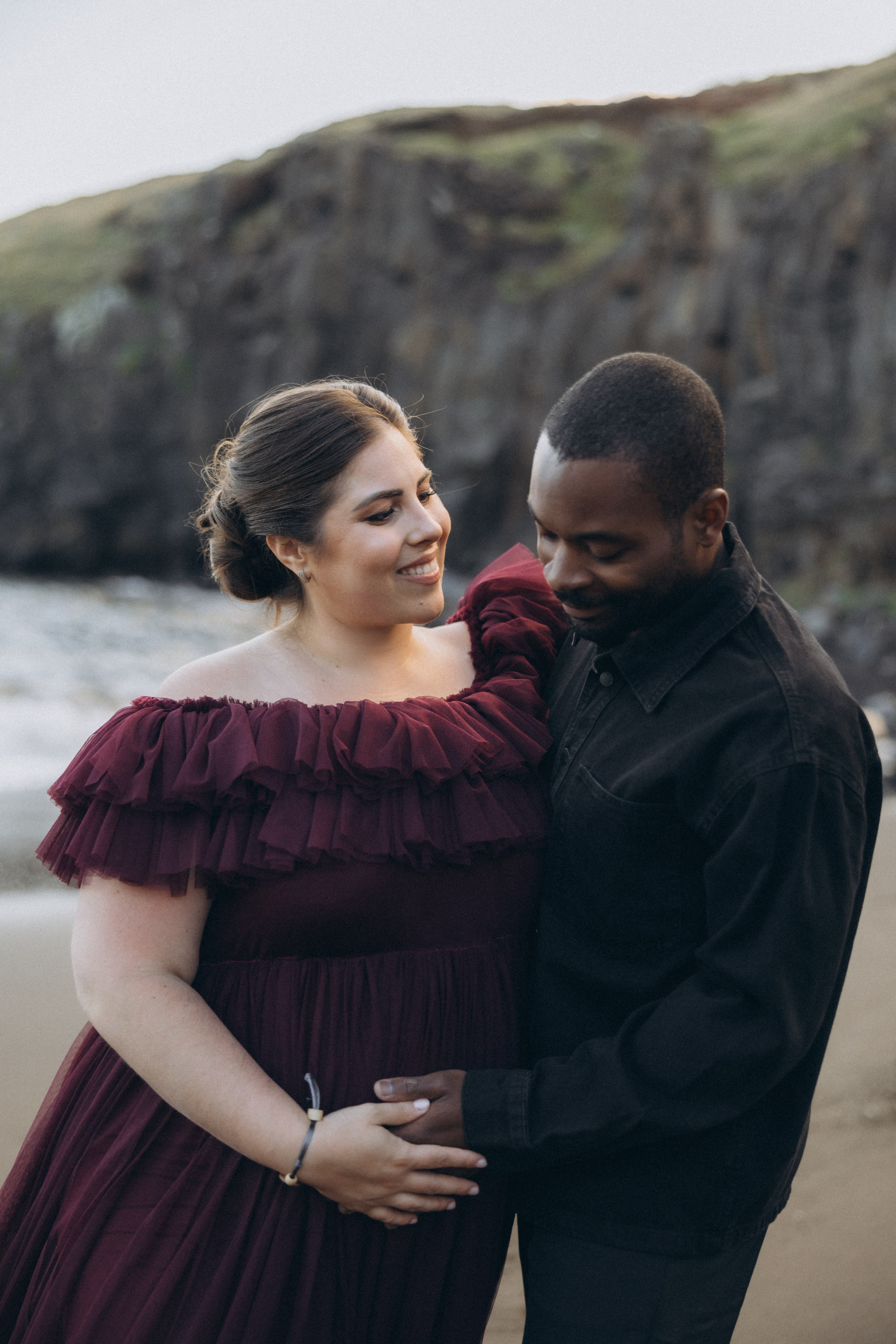 A glowing expectant mother standing on a cliff overlooking the ocean in Madeira, her dress flowing gently in the wind as the golden sunset casts a warm glow.