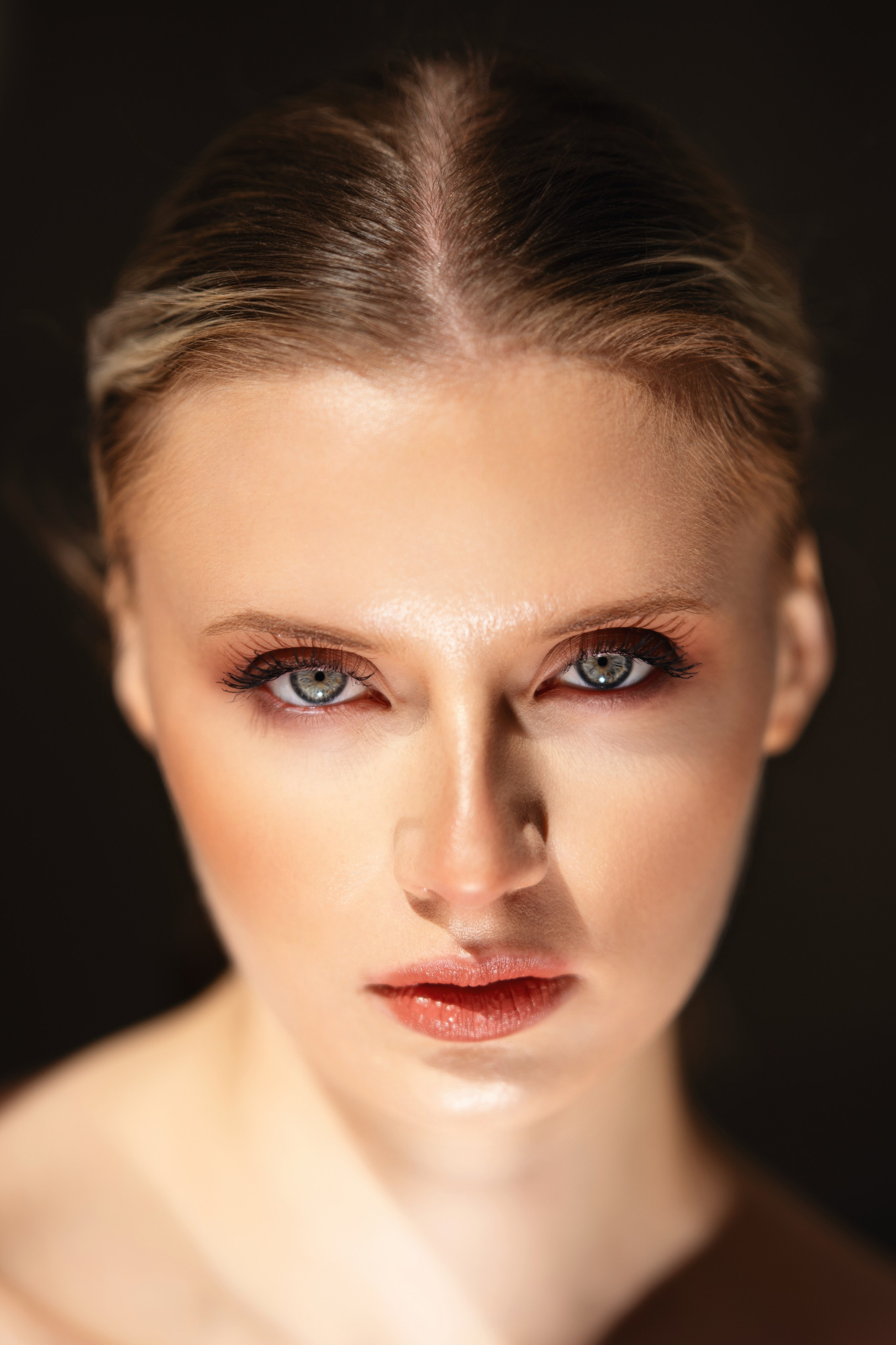 Close beauty portrait of a woman with slicked-back hair and direct gaze, photographed in clean light with a polished editorial finish.
