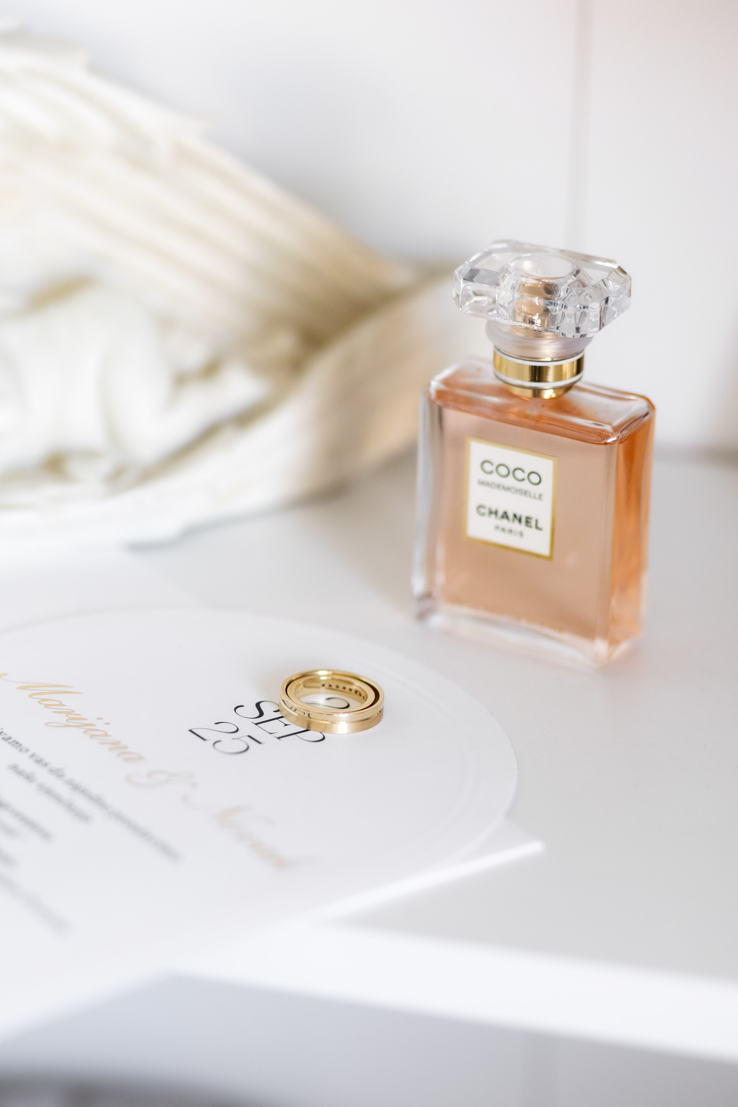 Wedding rings carefully arranged beside a luxury perfume and wedding invitation, capturing an elegant bridal flat lay during the wedding preparations.