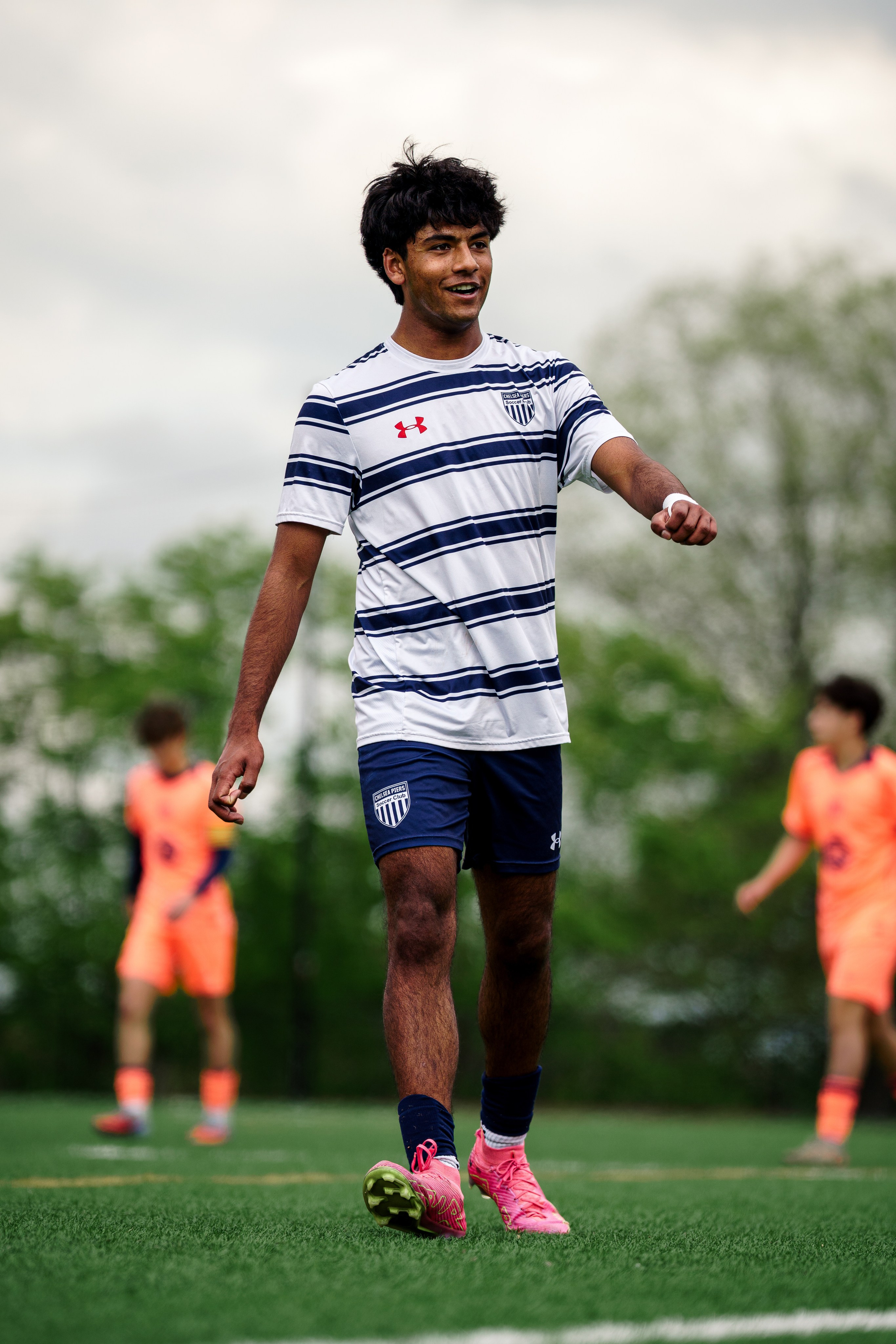 Youth soccer player in a striped jersey watching the play develop during a game. Smiling and showing emotion as they win. 