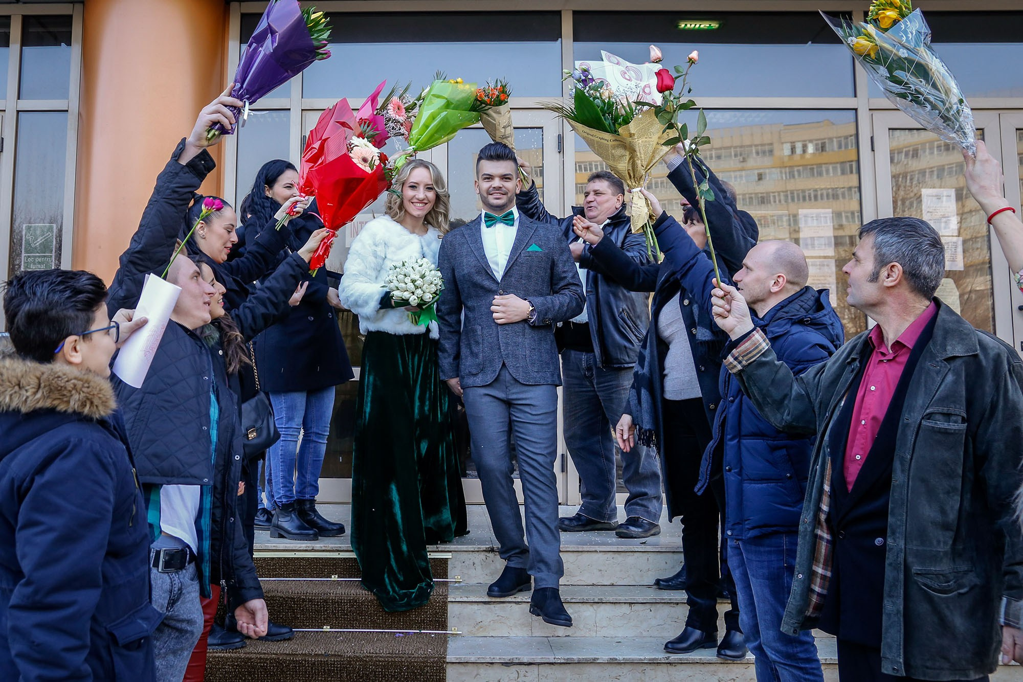 Wedding guests lined up at the town hall exit creating a tunnel of flowers for the newlyweds during a winter civil ceremony.
