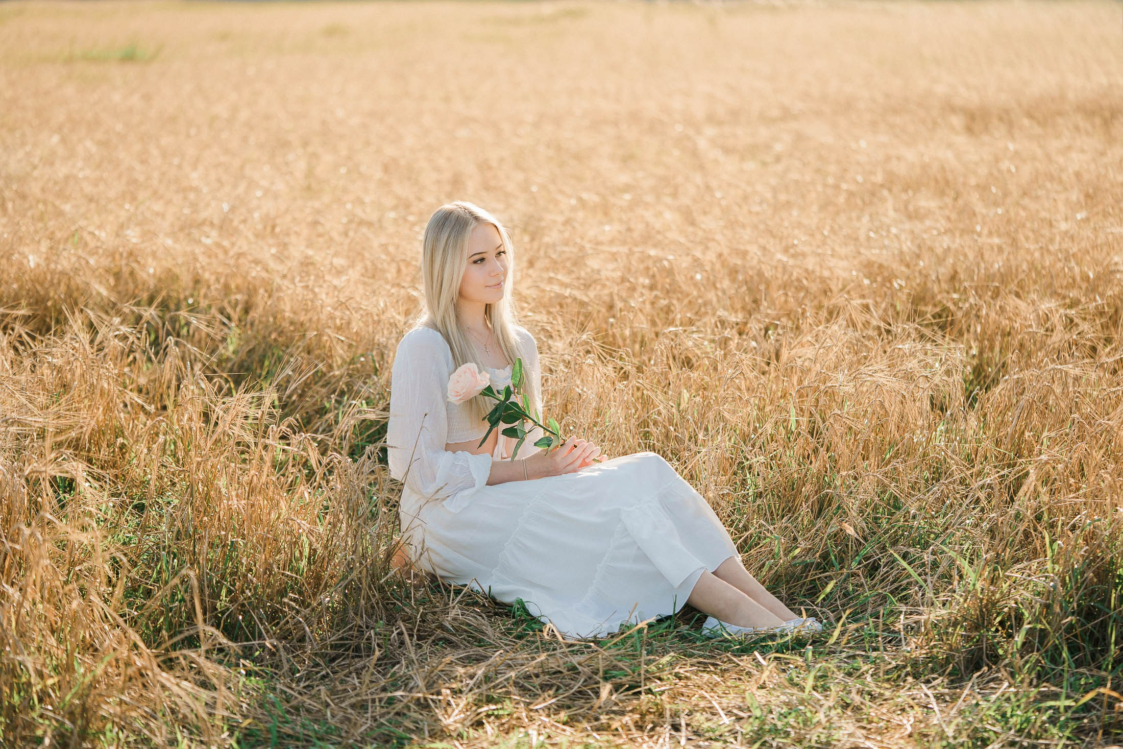 nuori nainen valkoisessa mekossa istuu pellolla kultaisessa ilta-auringossa
