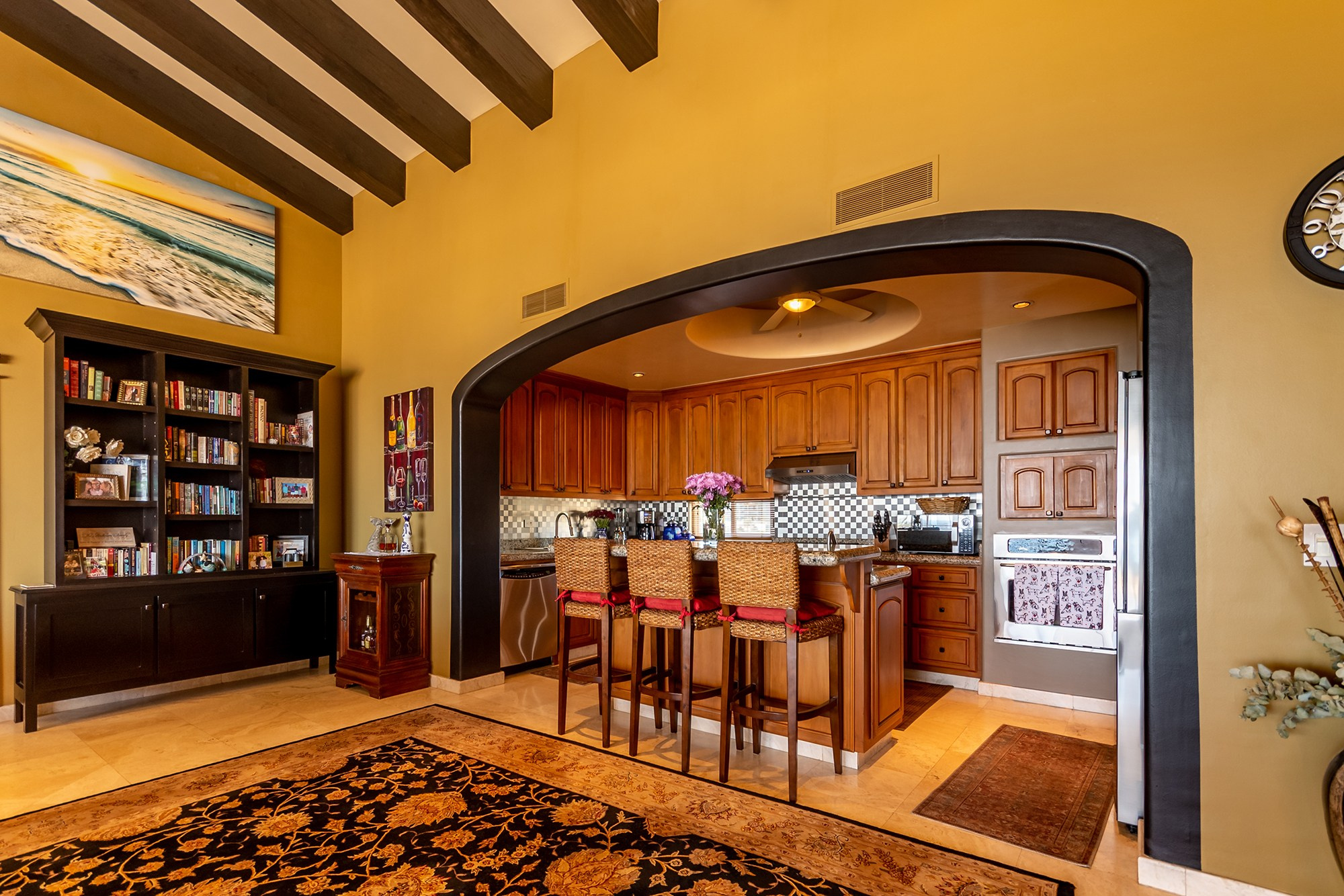Luxury home interior in Los Cabos – kitchen viewed through arch from living room, warm tones and elegant wood finishes