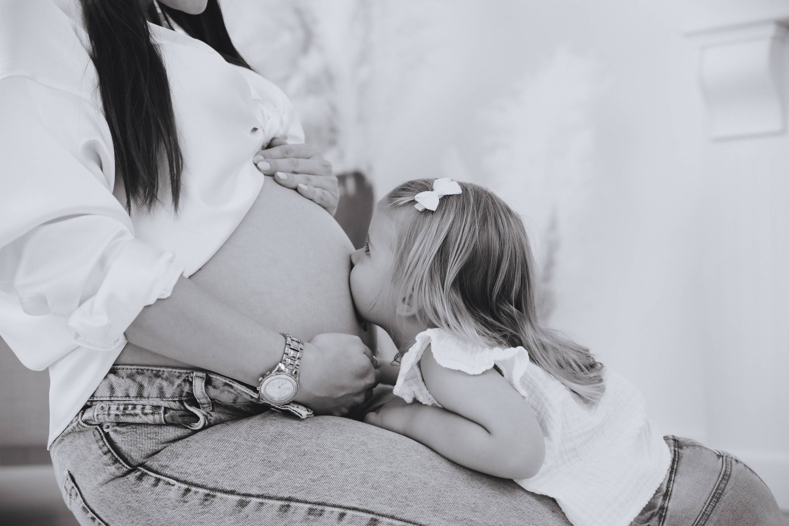 Mädchen küsst liebevoll den Babybauch ihrer schwangeren Mutter.