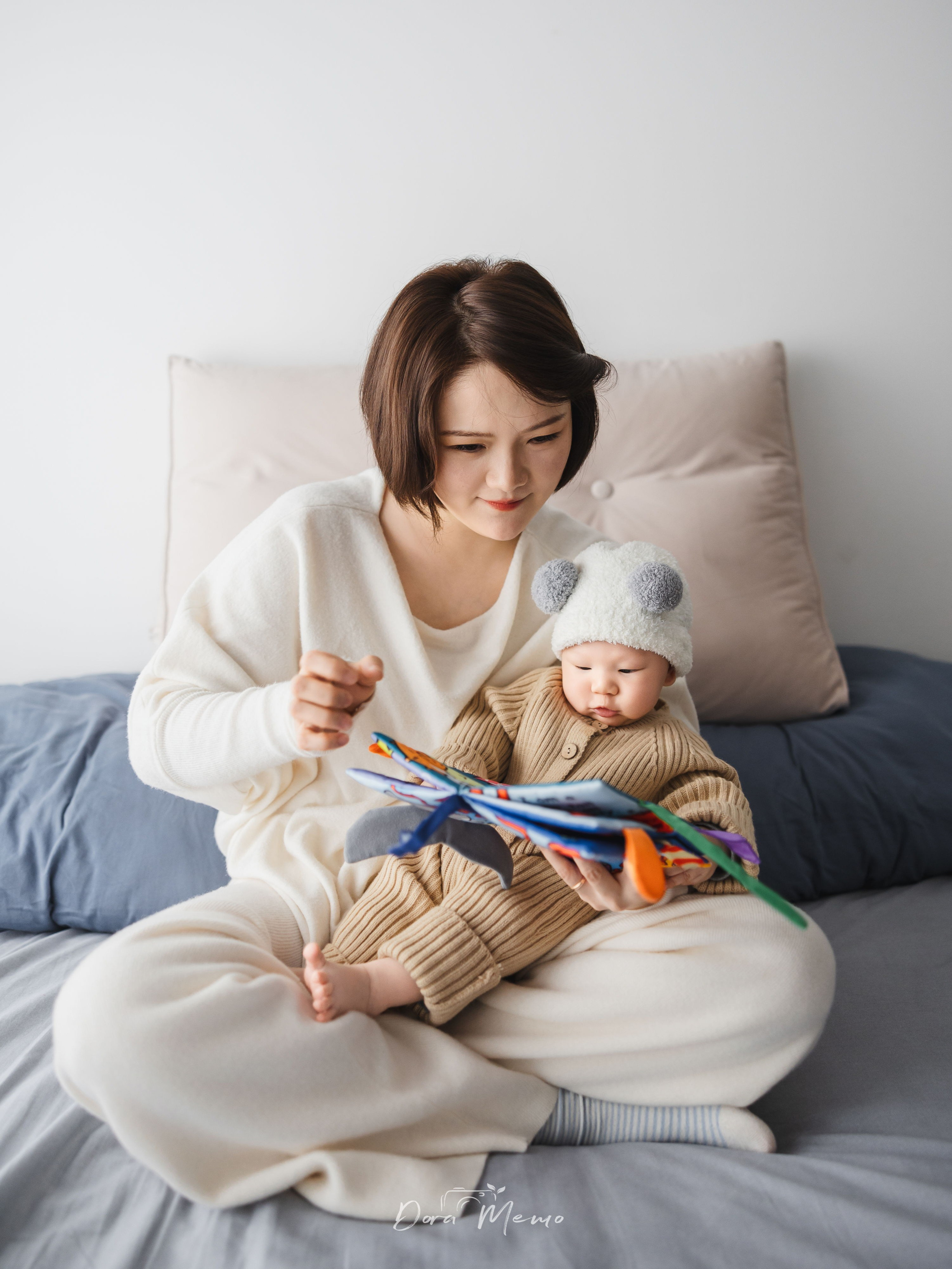 Mother and baby sitting on bed reading toy book, cozy home family photography