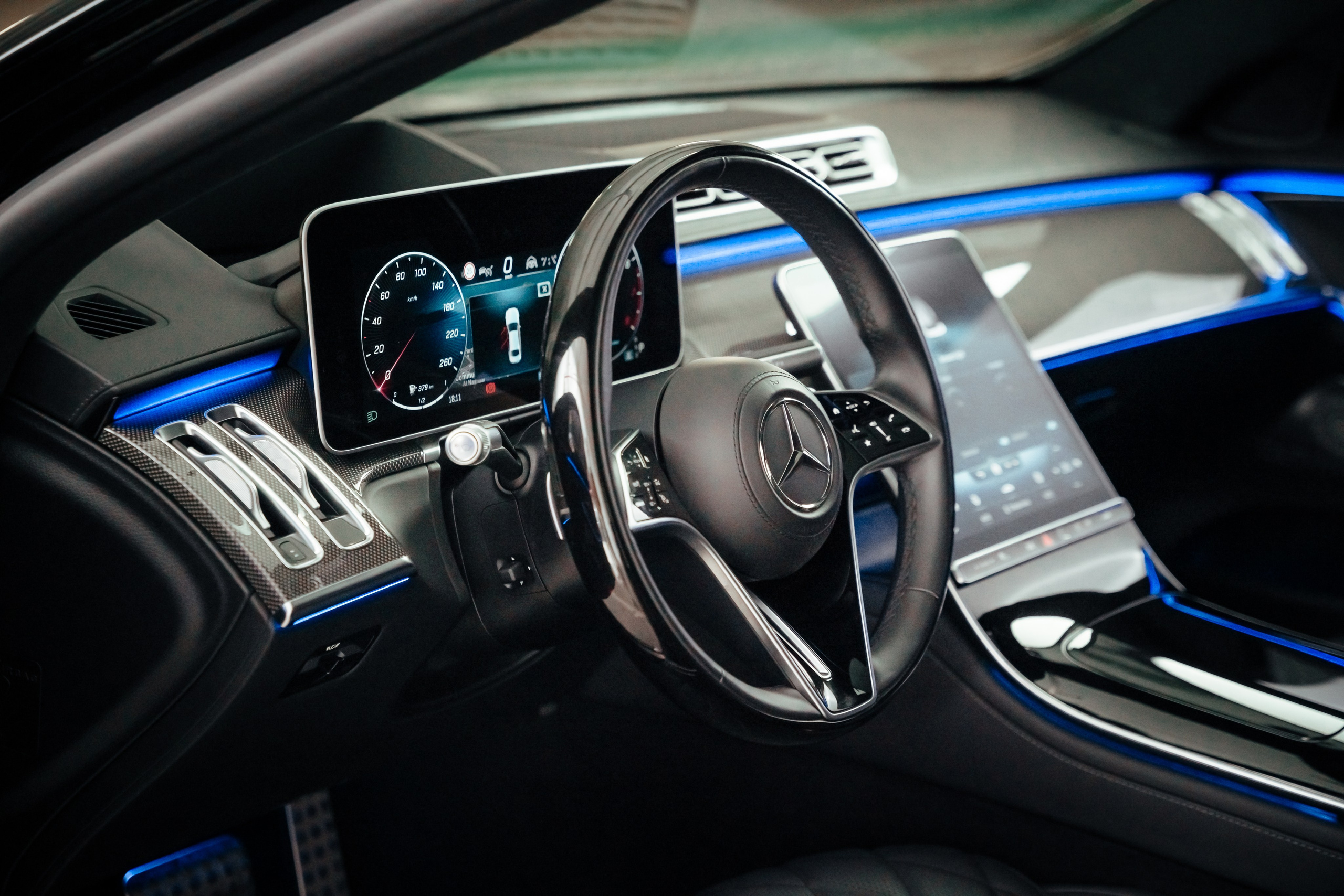 The interior is a dark-colored Mercedes steering wheel with neon lighting and carbon fiber cover
