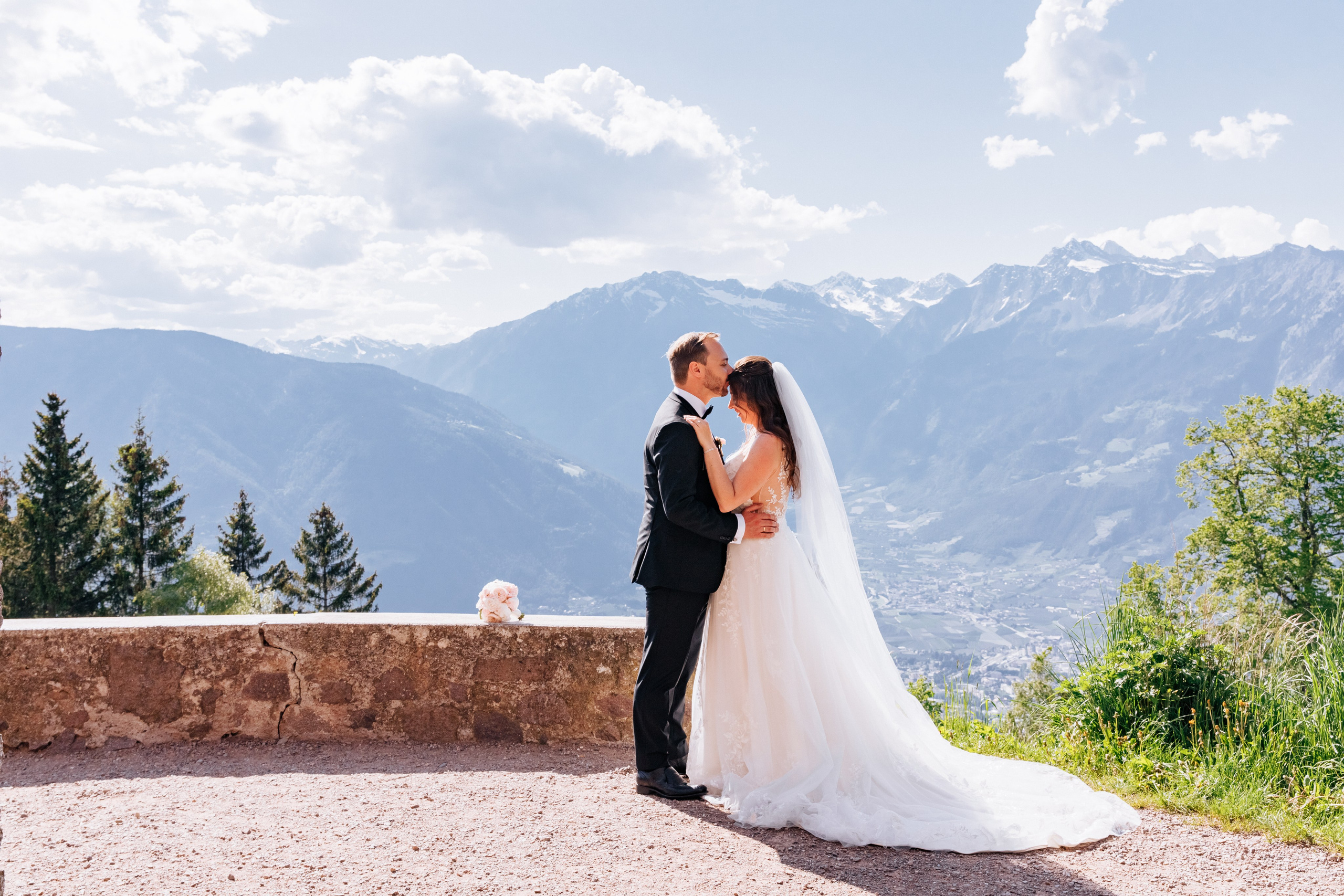 Der Bräutigam küsst die Braut liebevoll auf die Stirn vor der malerischen Bergpanorama Südtirols.