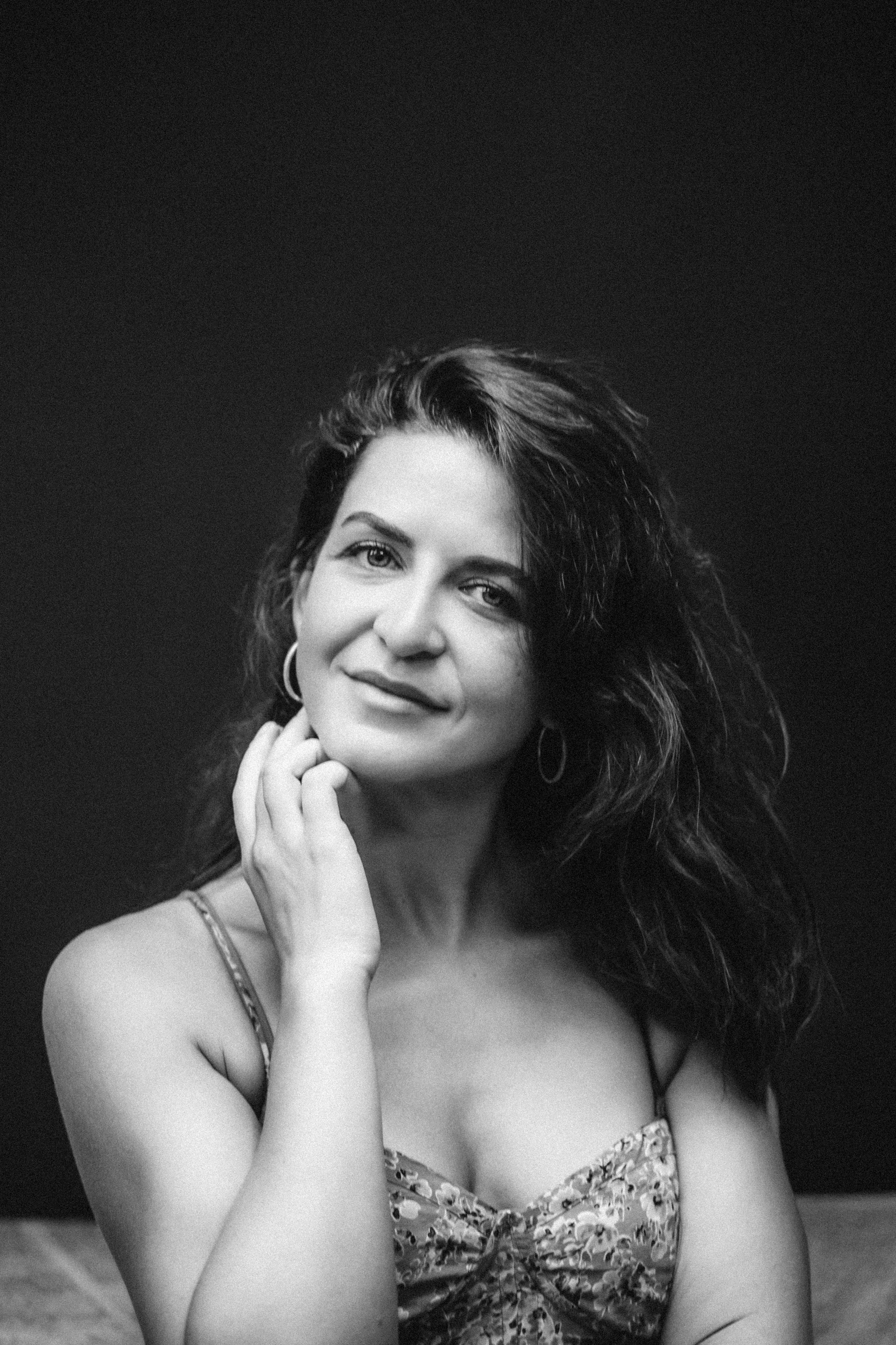 Чёрно-белый женский портрет, снятый в Валенсии, Испания, с элегантной женщиной с естественными кудрями и мягким, уверенным выражением лица на тёмном фоне, подчёркивающим вневременную красоту и эмоции — идеально для женских фотосессий в Валенсии, художественных чёрно-белых портретов и профессиональной женской фотографии по всей Испании.