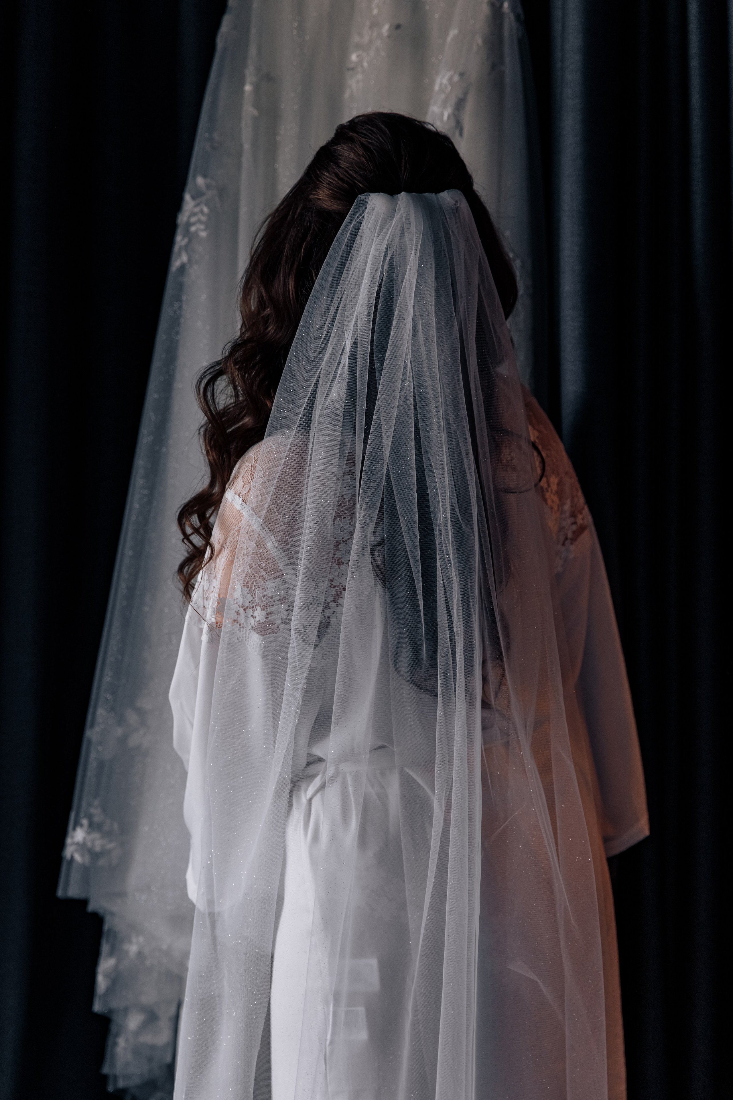 Die Braut steht mit dem Rücken zu uns, wobei ihr Schleier deutlich sichtbar ist. 