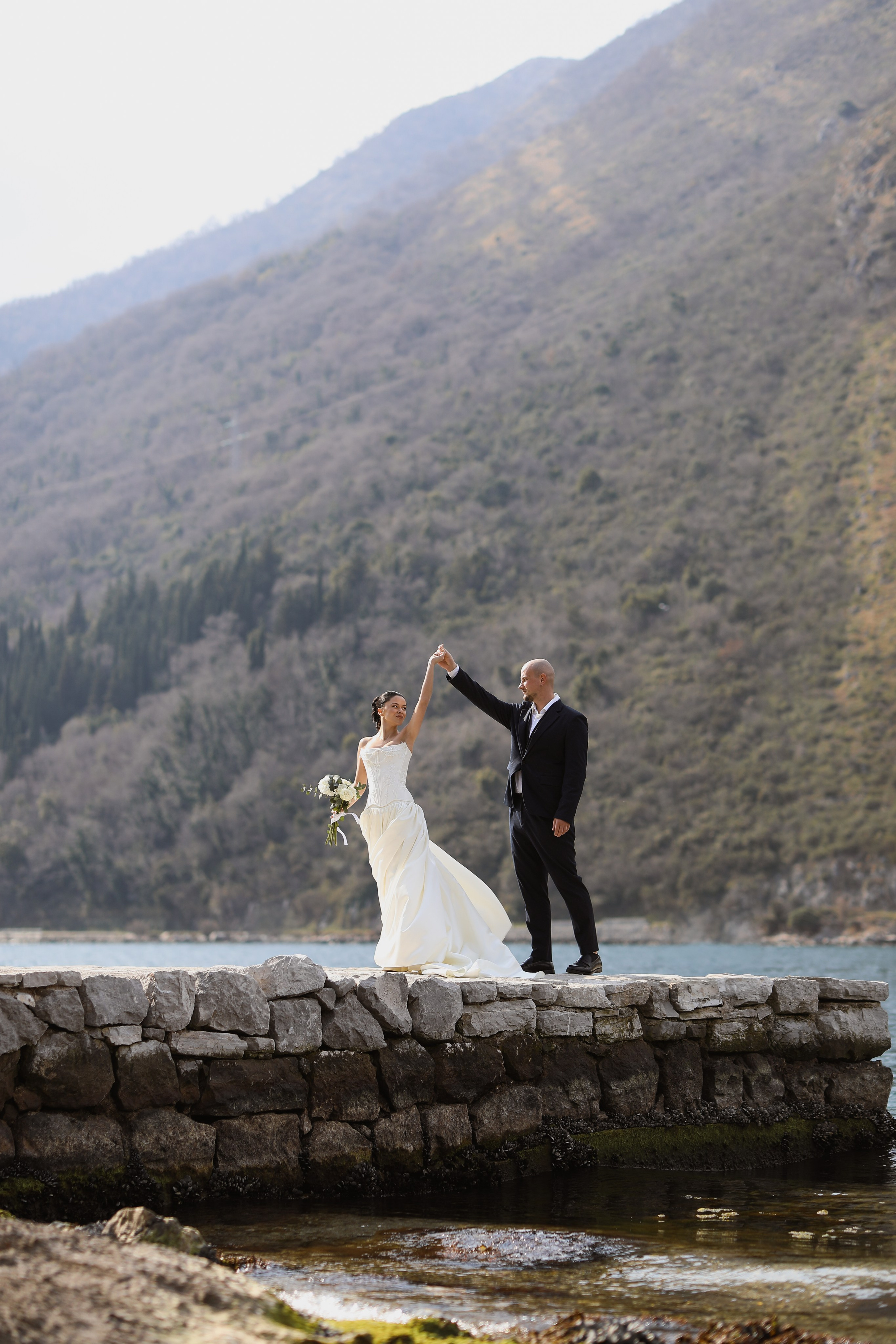 Bride and groom dancing on a stone pier with mountains in Italy during wedding photoshoot