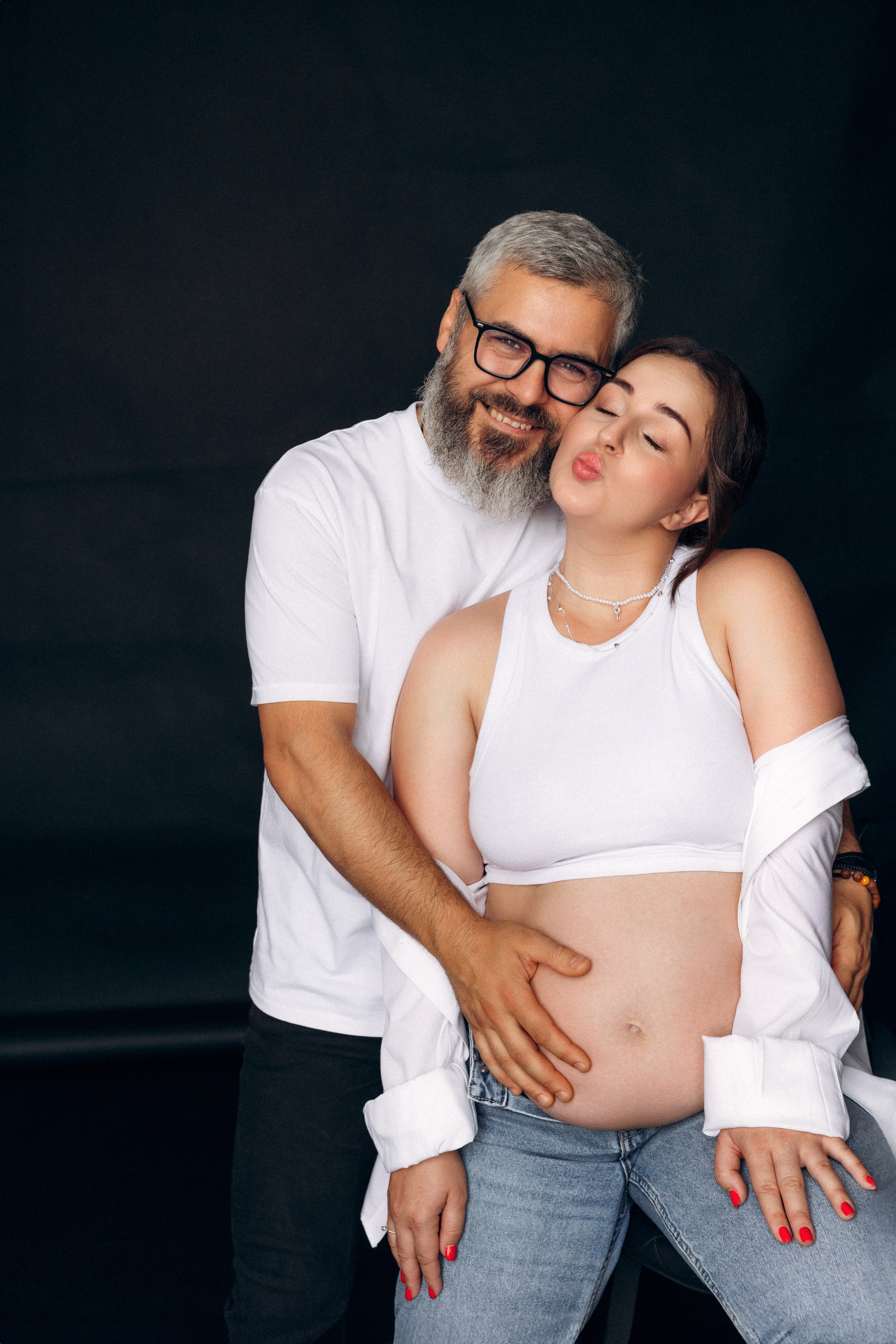  Czułość i spokój – partner całuje ciężarną kobietę w czoło, pełne miłości zdjęcie z sesji ciążowej.